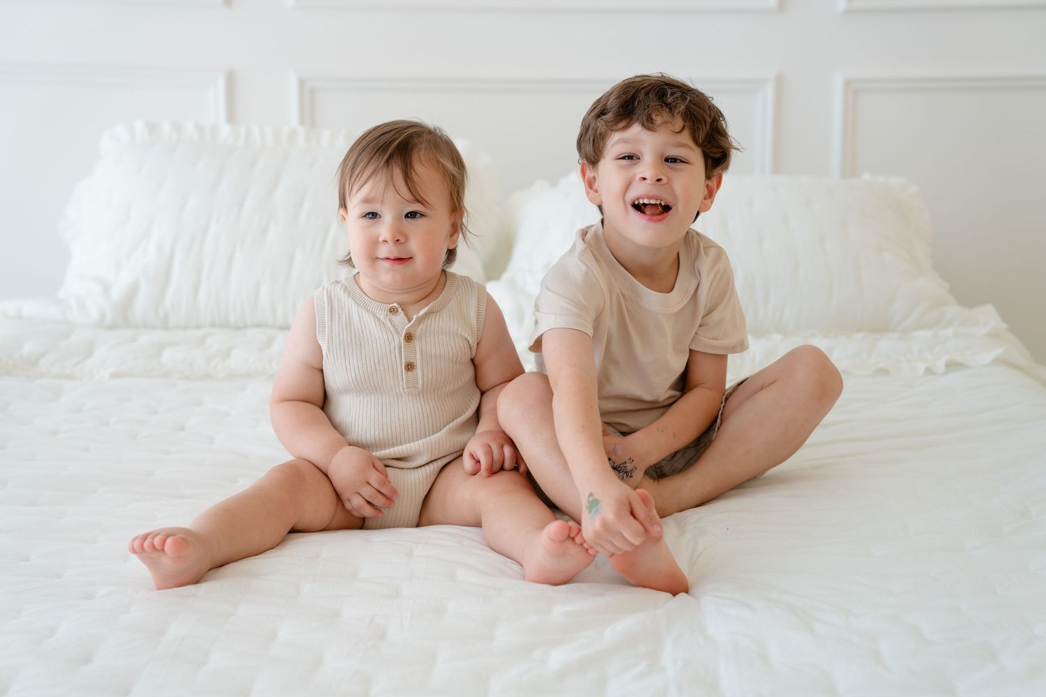 Smiling baby in blue striped romper with number 1 applique sits between white curtains in bright natural light.