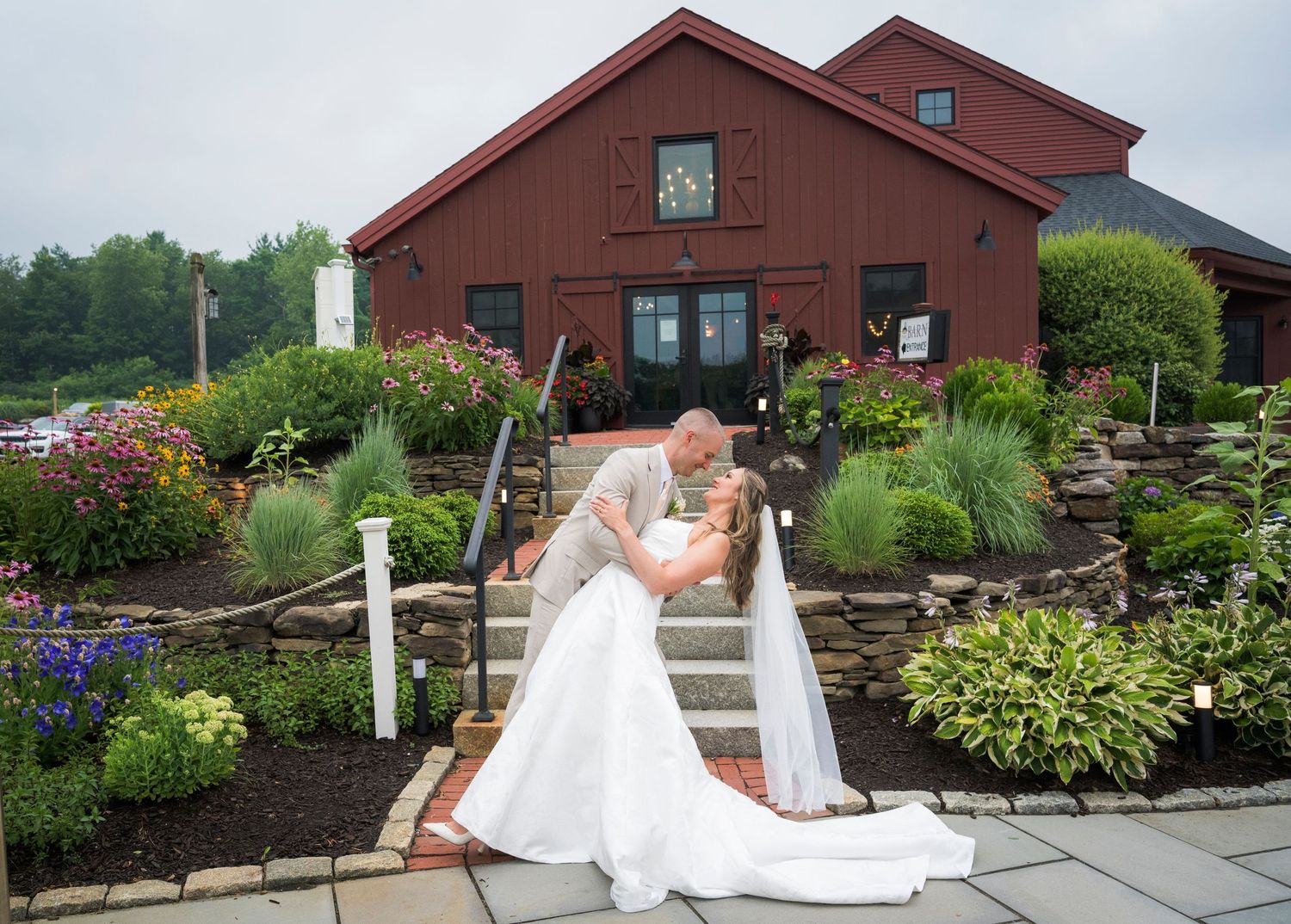 A winter wedding portrait outside a white farmhouse with illuminated windows and a full moon.
