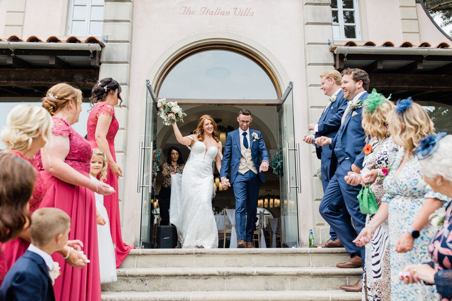 Wedding guests gather outside a stone building entrance during a joyful celebration.