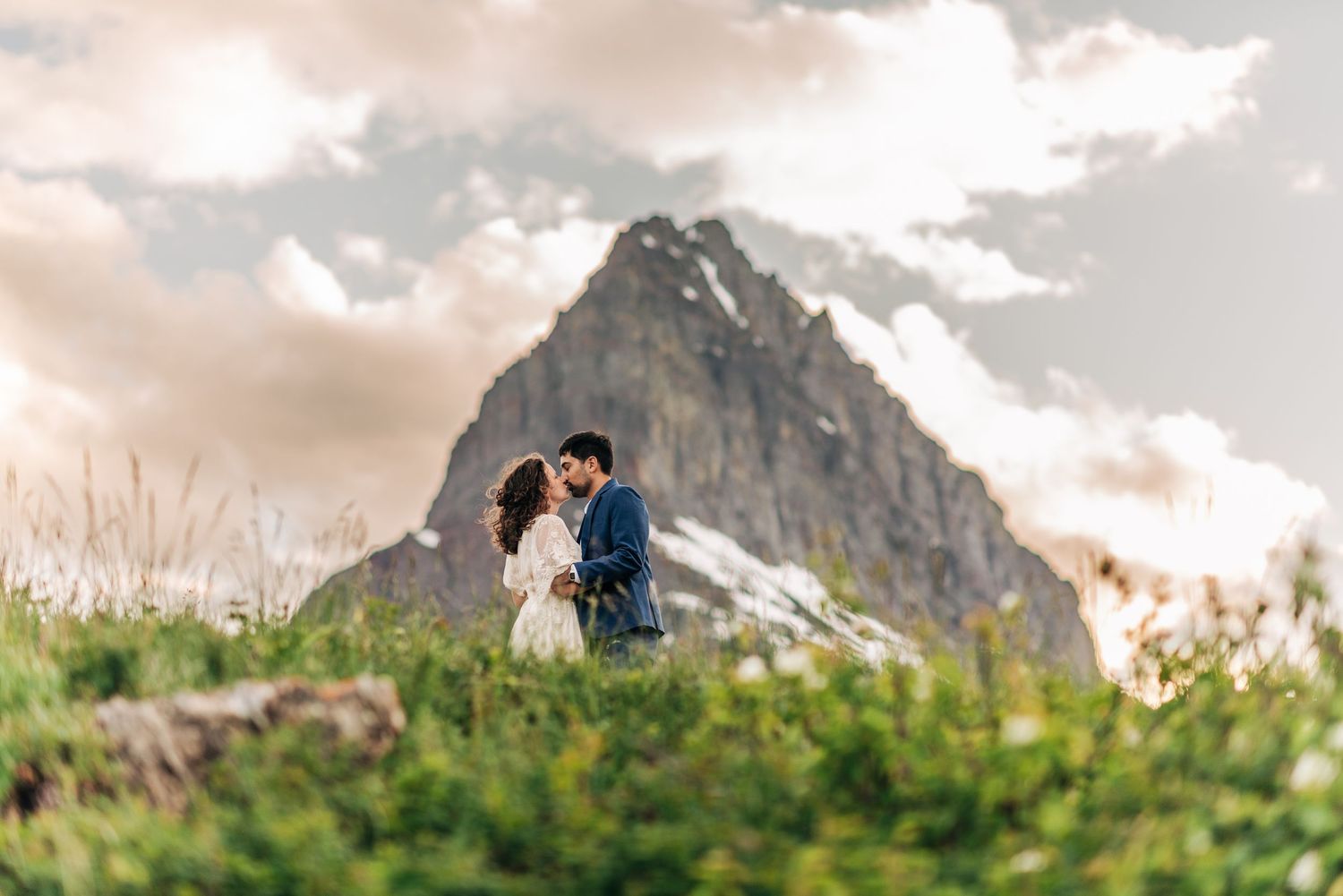 A couple embraces on a hilltop overlooking a scenic mountain landscape during golden hour.