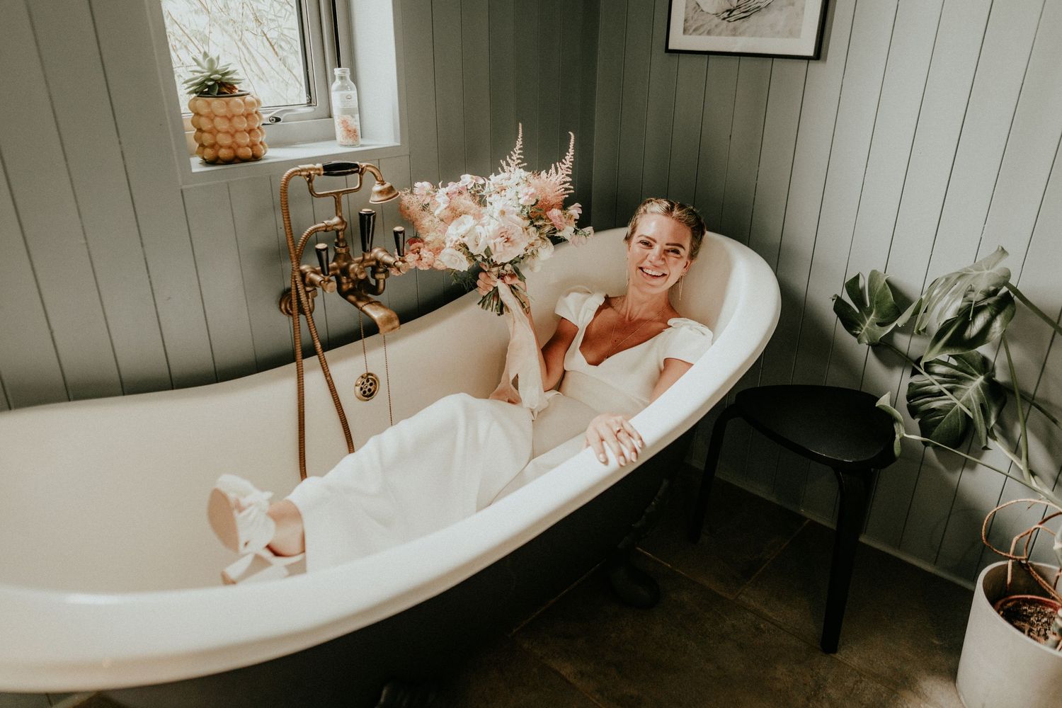 Vintage clawfoot bathtub in sage green bathroom with dried flowers and potted plants creating a relaxing spa atmosphere.