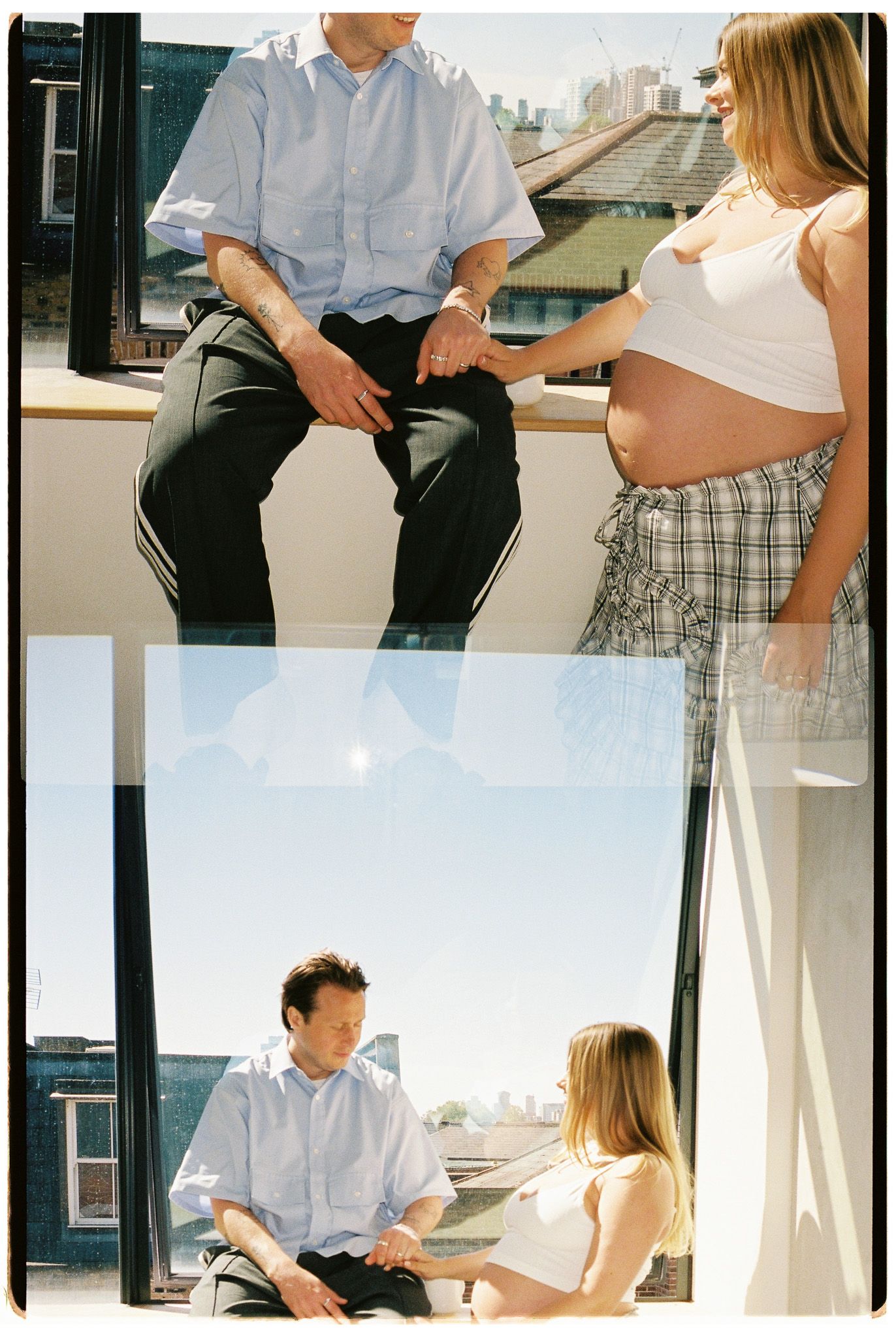 Couple sharing a tender moment by a sunny window, woman with pregnant belly holding hands with seated man.
