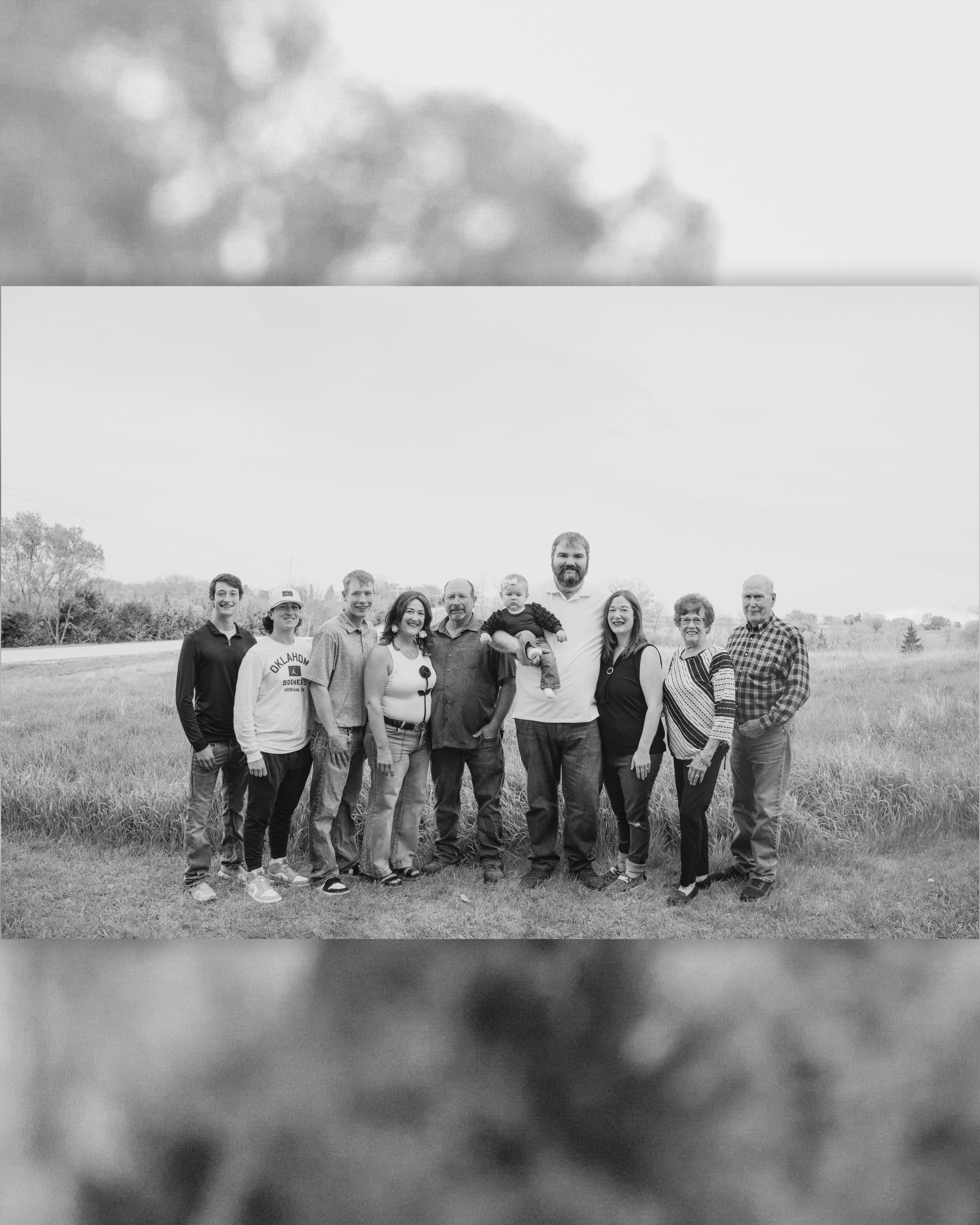 A group of eleven people posing together in a grassy field for a black and white family portrait outdoors.