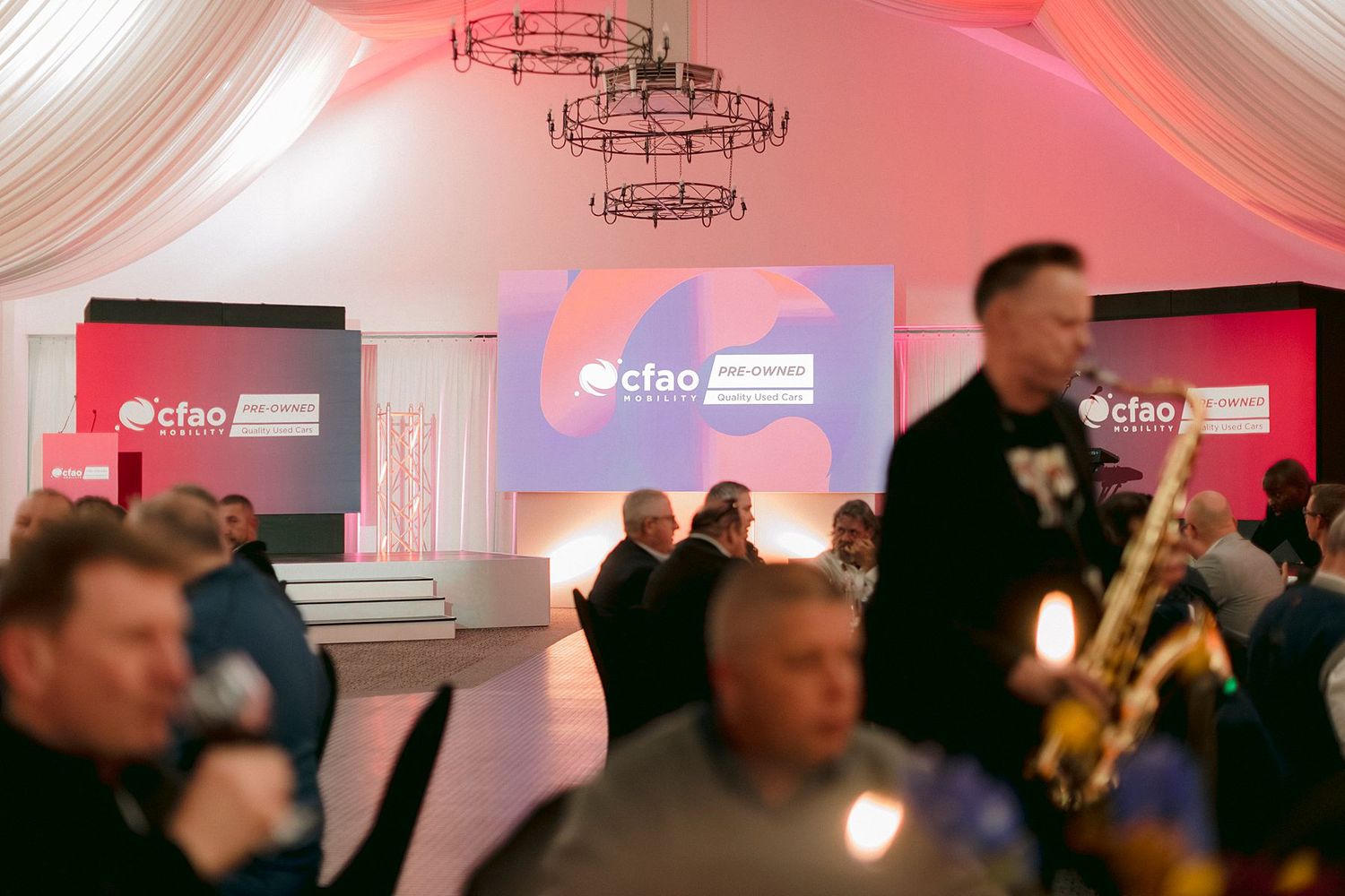 CFAO corporate event in elegant draped venue with guests networking, live saxophone music, and branded display screens.