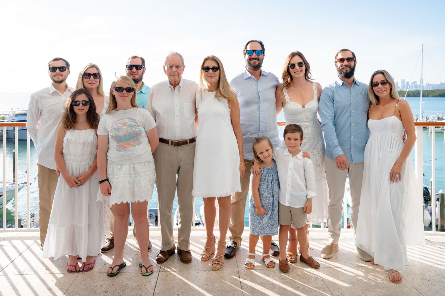 Large family group posing together on a sunny dock, dressed in coordinating white and light blue outfits for a special occasion.