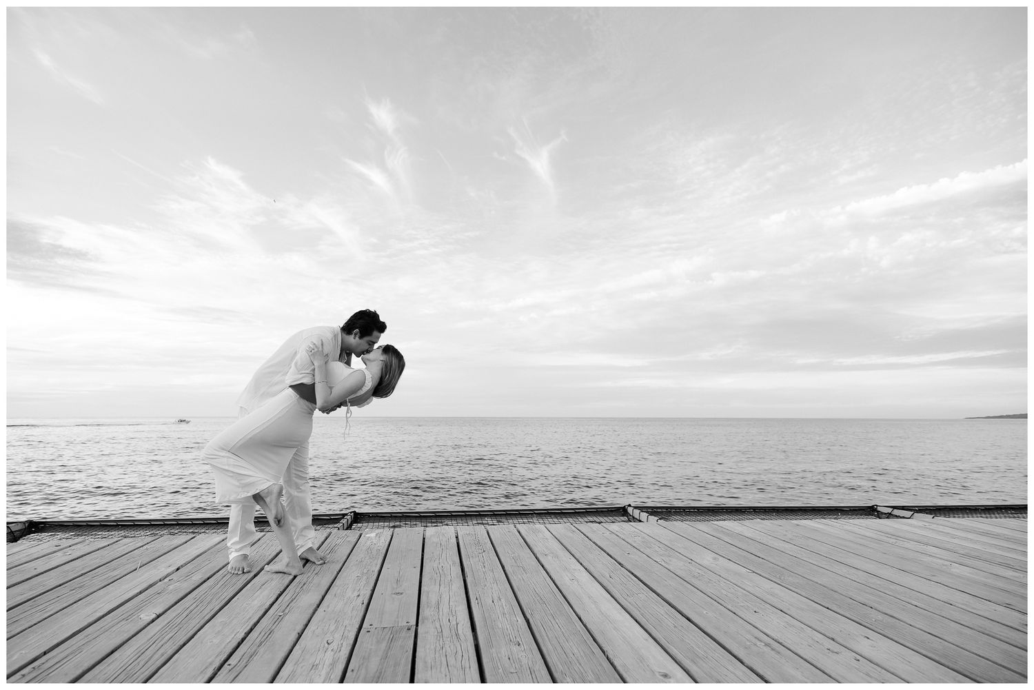 One & Only Mandarina engagement photos of couple sharing a dip kiss on a wooden pier overlooking the ocean.