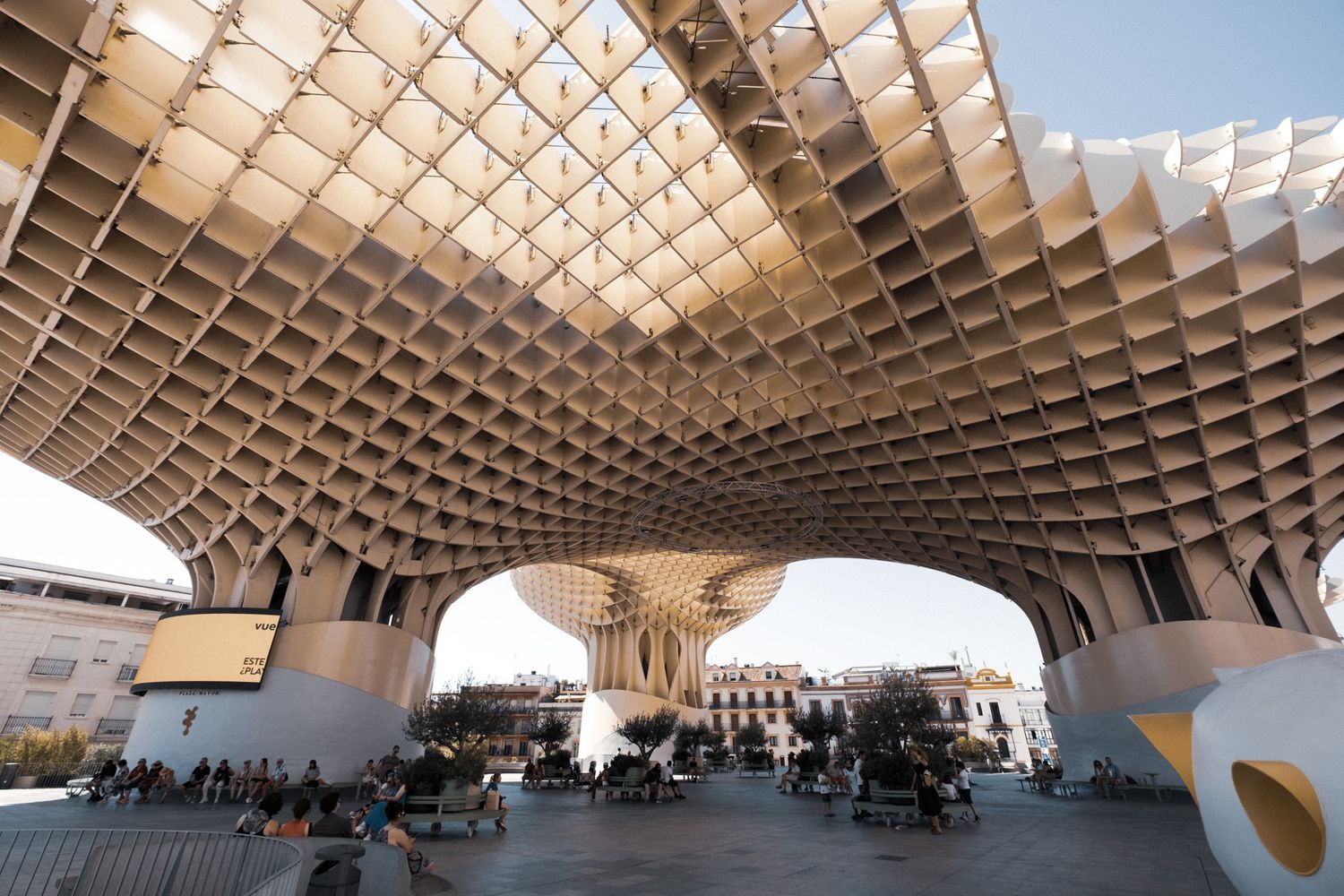 Close-up view of the Metropol Parasol structure in Seville, Spain, featuring its distinctive latticed wooden canopy against a blue sky.