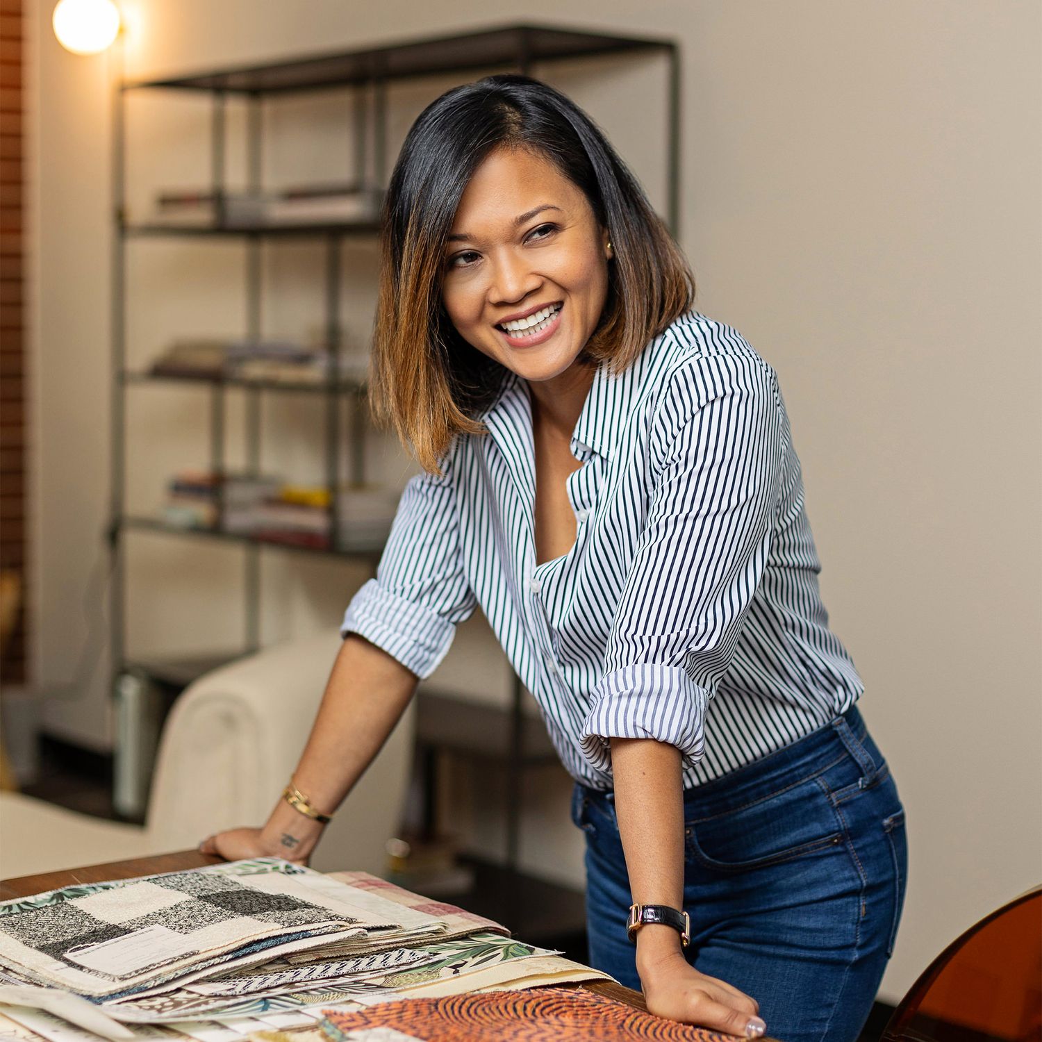 Person in striped shirt and jeans working at desk with architectural drawings.