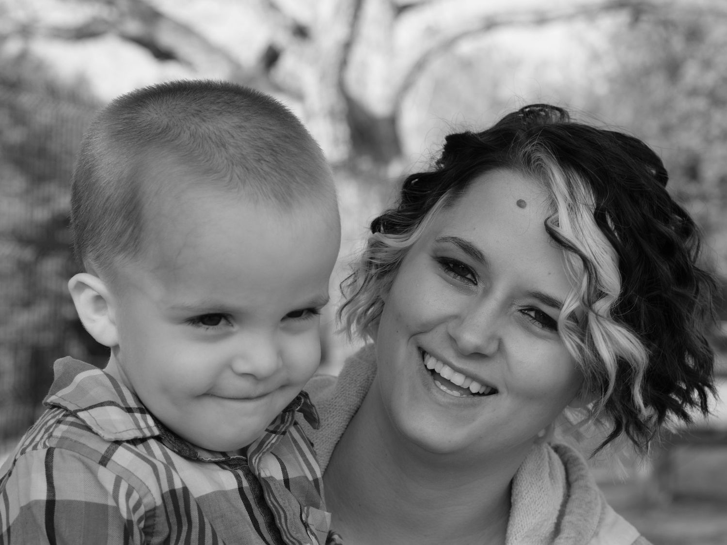 Black and white portrait of a smiling young woman with curly hair posing with a young boy outdoors.