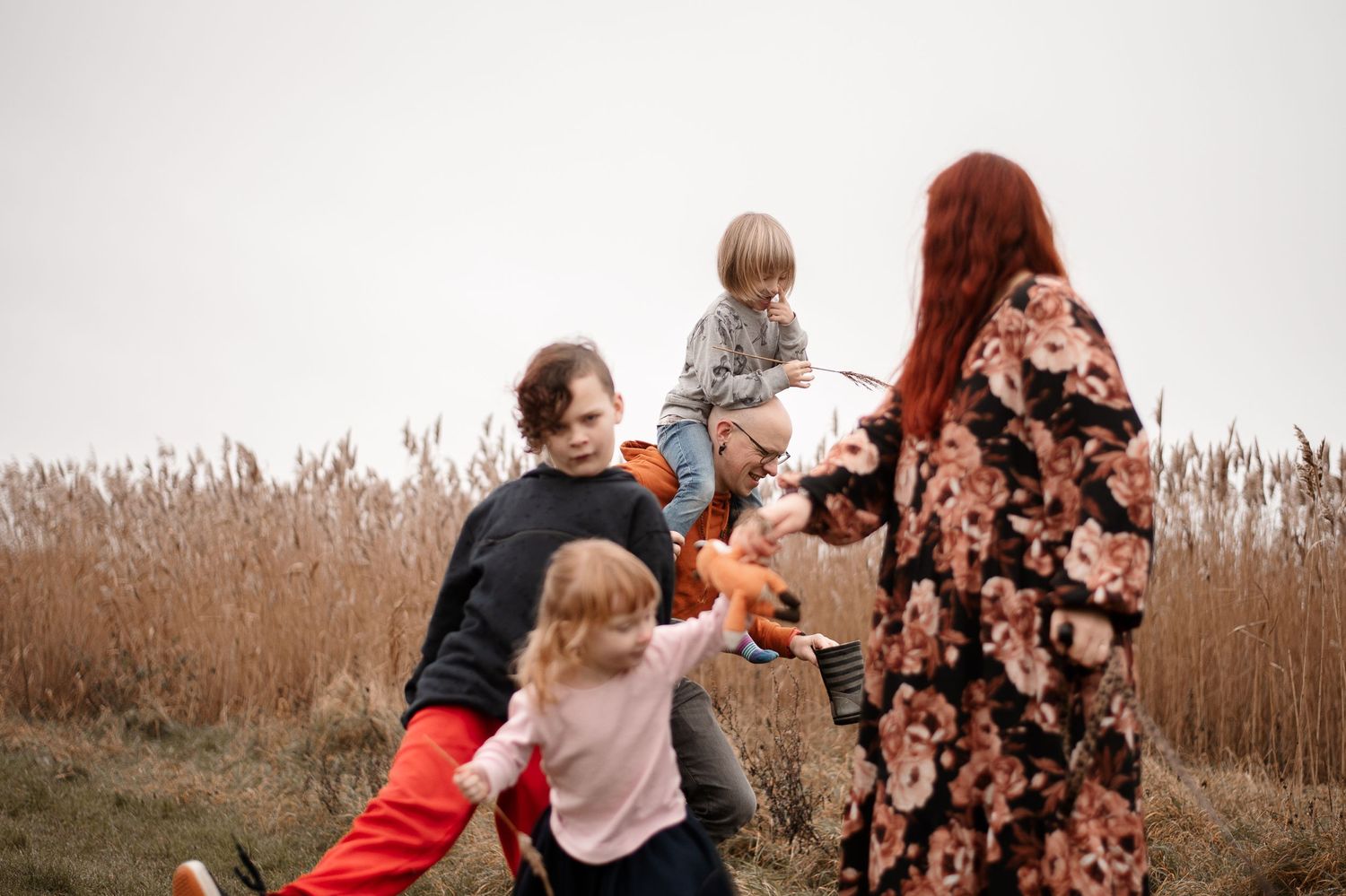 Family gathering in tall grass field during overcast day.