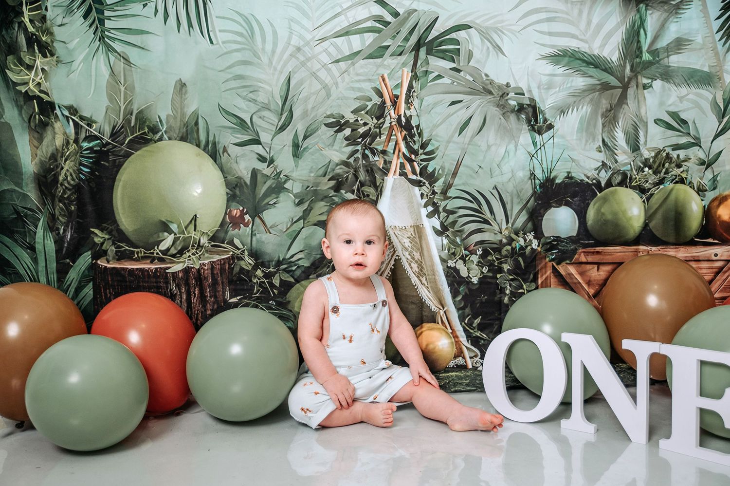 Safari-themed first birthday photo with decorative teepee and colorful balloons.