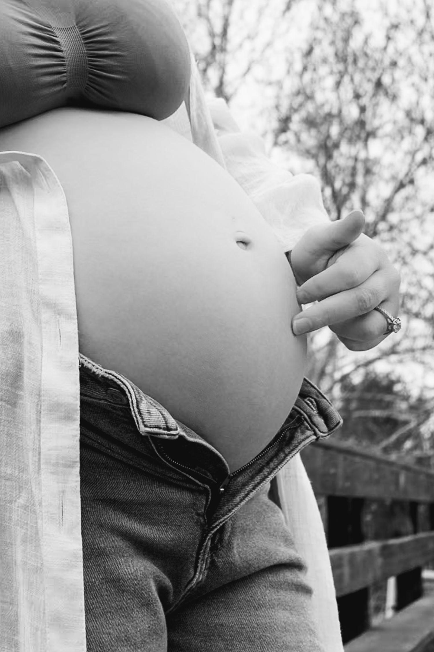 Black and white close-up photograph of pregnant belly with hands resting gently on bump.