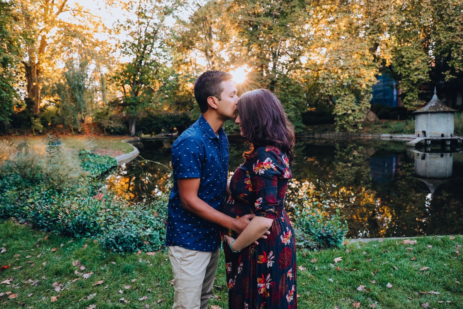 Intimate maternity photoshoot in autumn park with couple embracing near water.