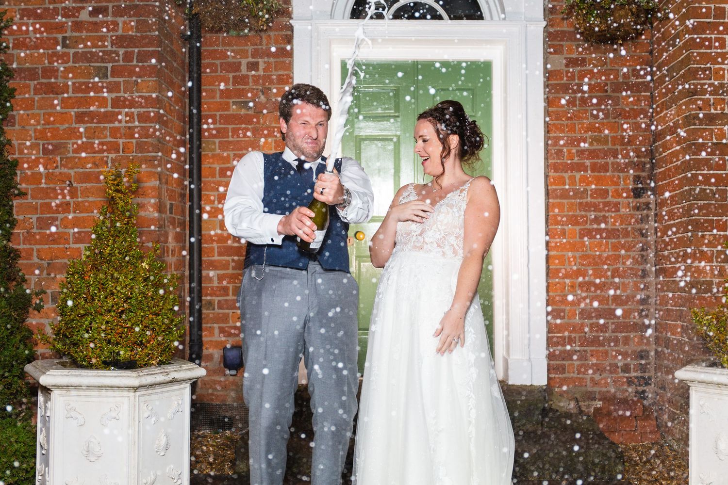 Wedding couple celebrating in the snow outside a red brick building entrance.