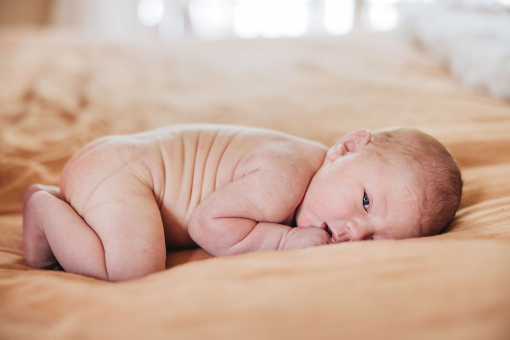 Newborn baby lying on side on beige blanket in natural light.