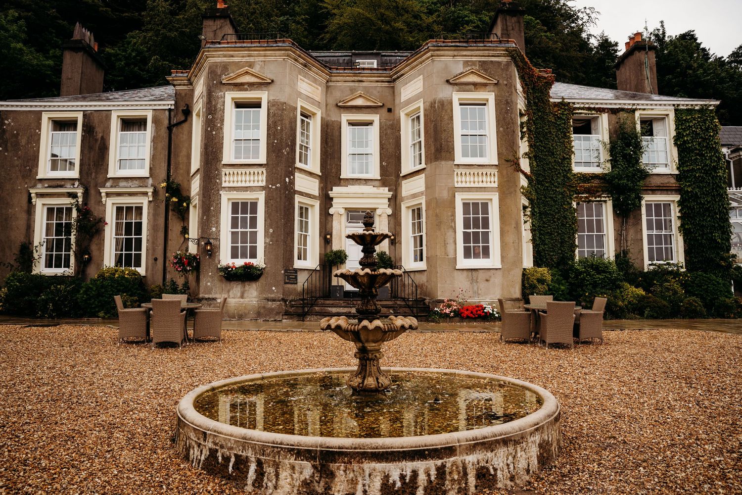 Elegant stone mansion with fountain in foreground and gravel driveway.