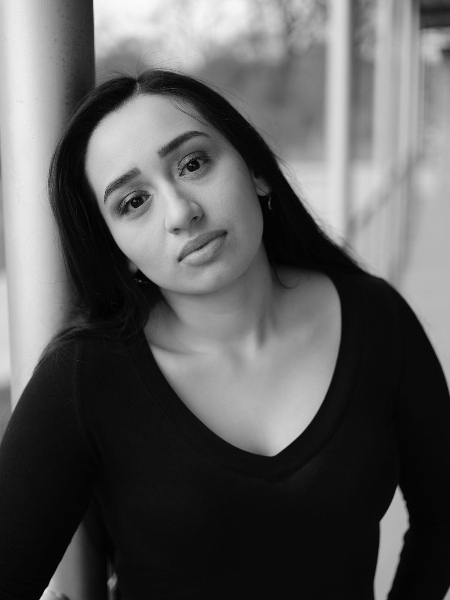 Black and white portrait of a young woman with long dark hair wearing a black top indoors.