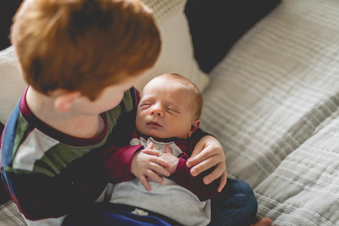 toddler brother holding his newborn brother on the bed