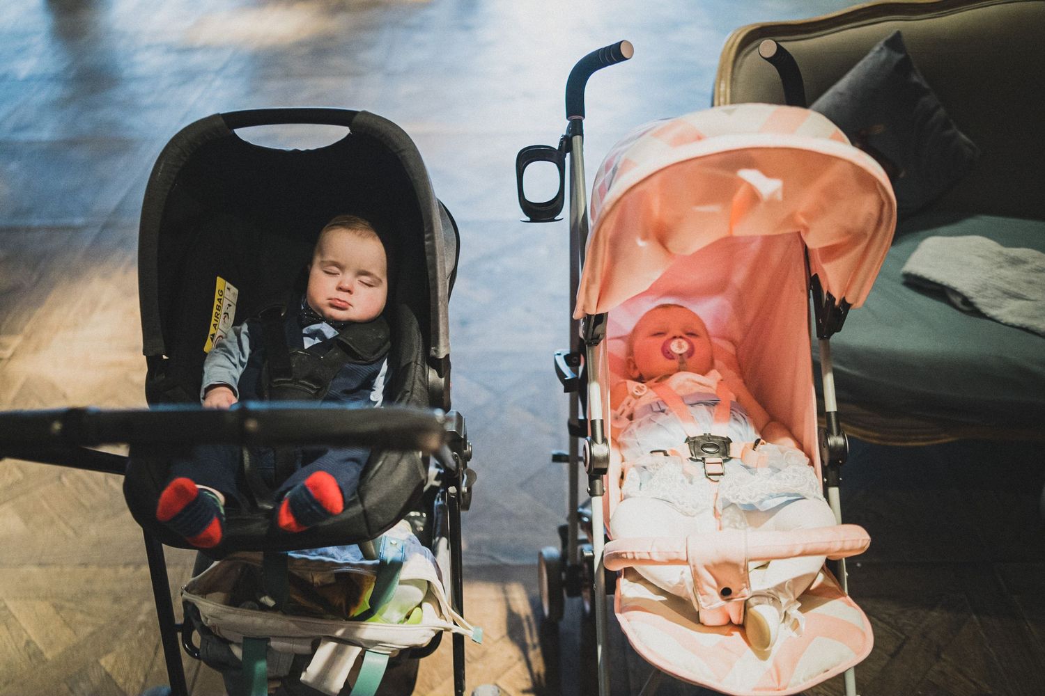 Two baby strollers parked side by side, one black and one coral pink.