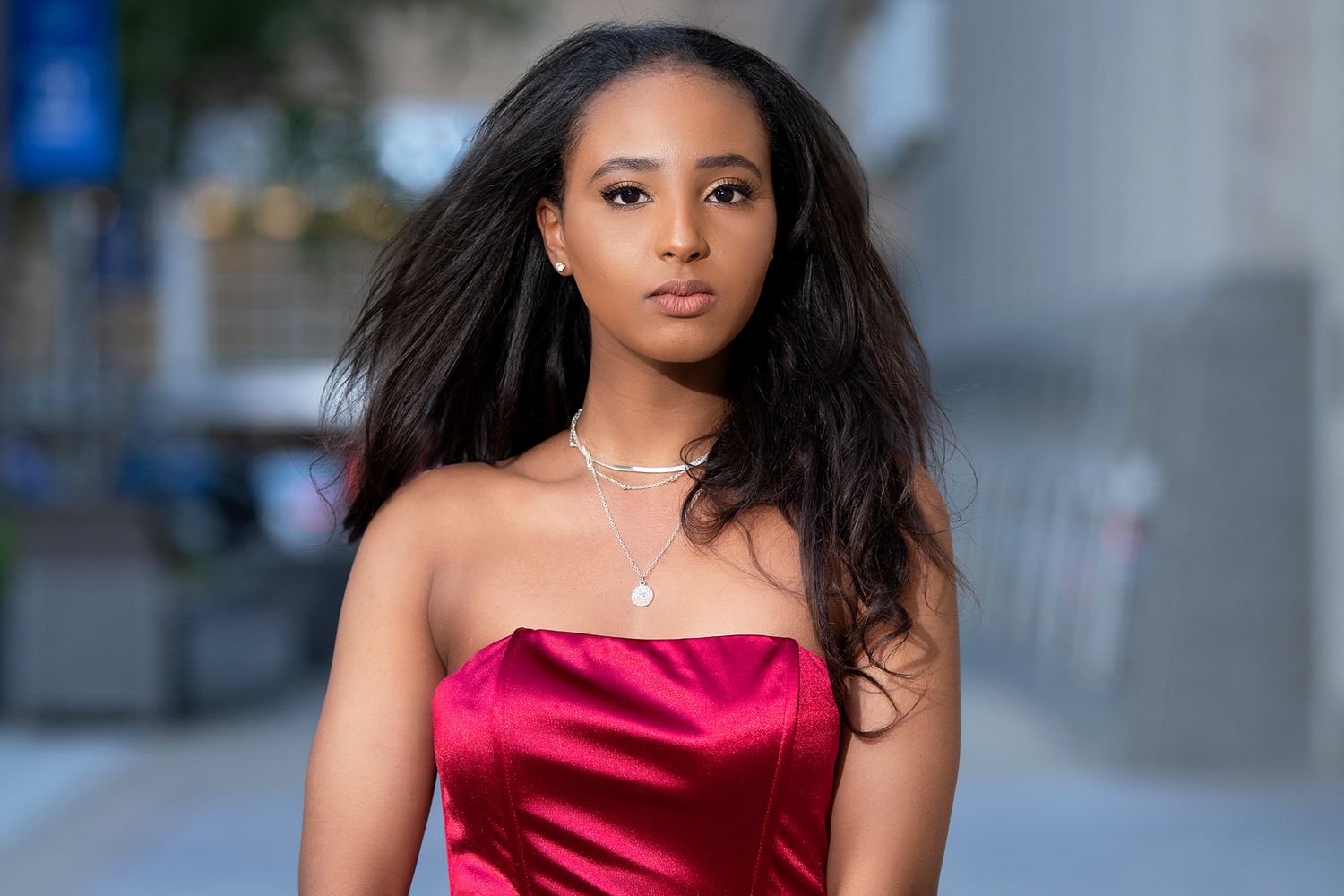 Portrait in red satin dress with urban background and soft lighting.