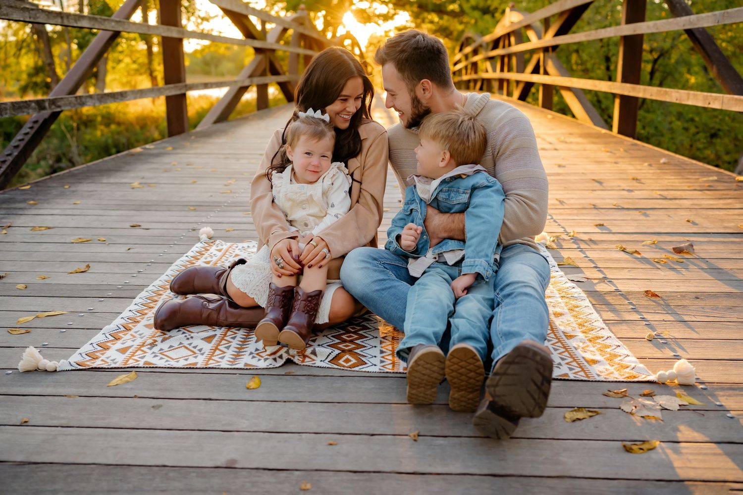Family sitting together on a wooden boardwalk during golden hour sunset in a park setting.