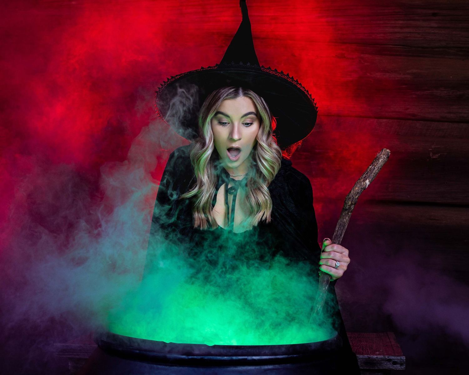 A witch in black hat stirs a bubbling green potion in a cauldron surrounded by mystical red smoke.