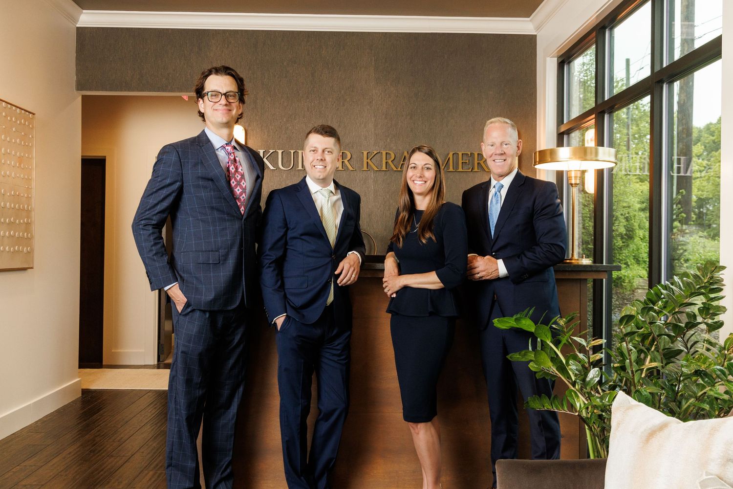 Professional business team in navy suits standing together in modern office lobby with wood floors and large windows. Grand Rapids Headshots