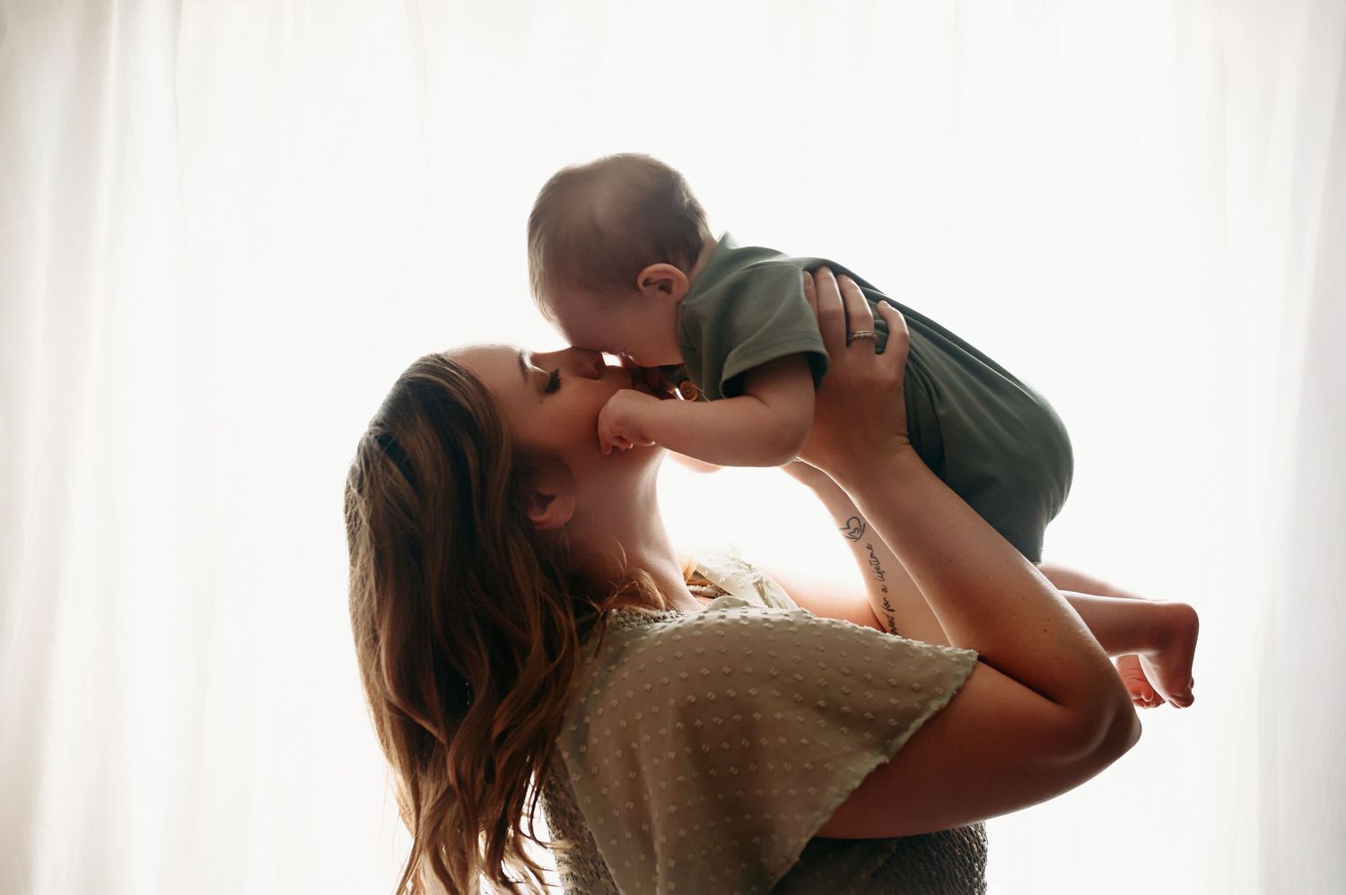 A series of silhouetted tender moments between a couple kissing and embracing in front of a bright window.