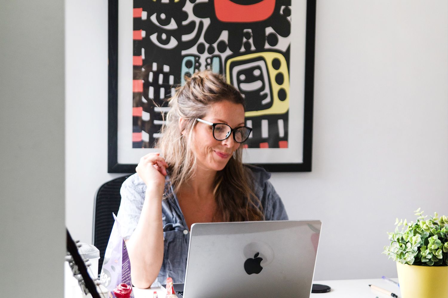 Person working at modern desk setup with Apple computer monitor and keyboard in bright home office environment.