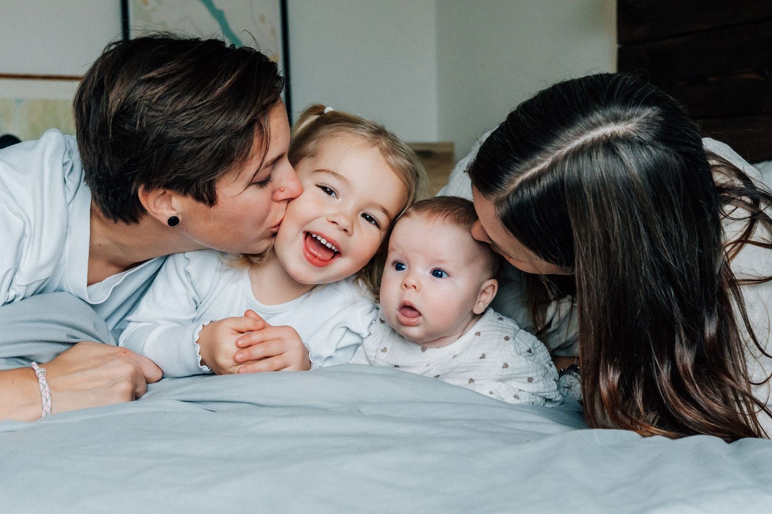 Familjen ligger på sängen och gosar under familjefotograferingen i hemmet.