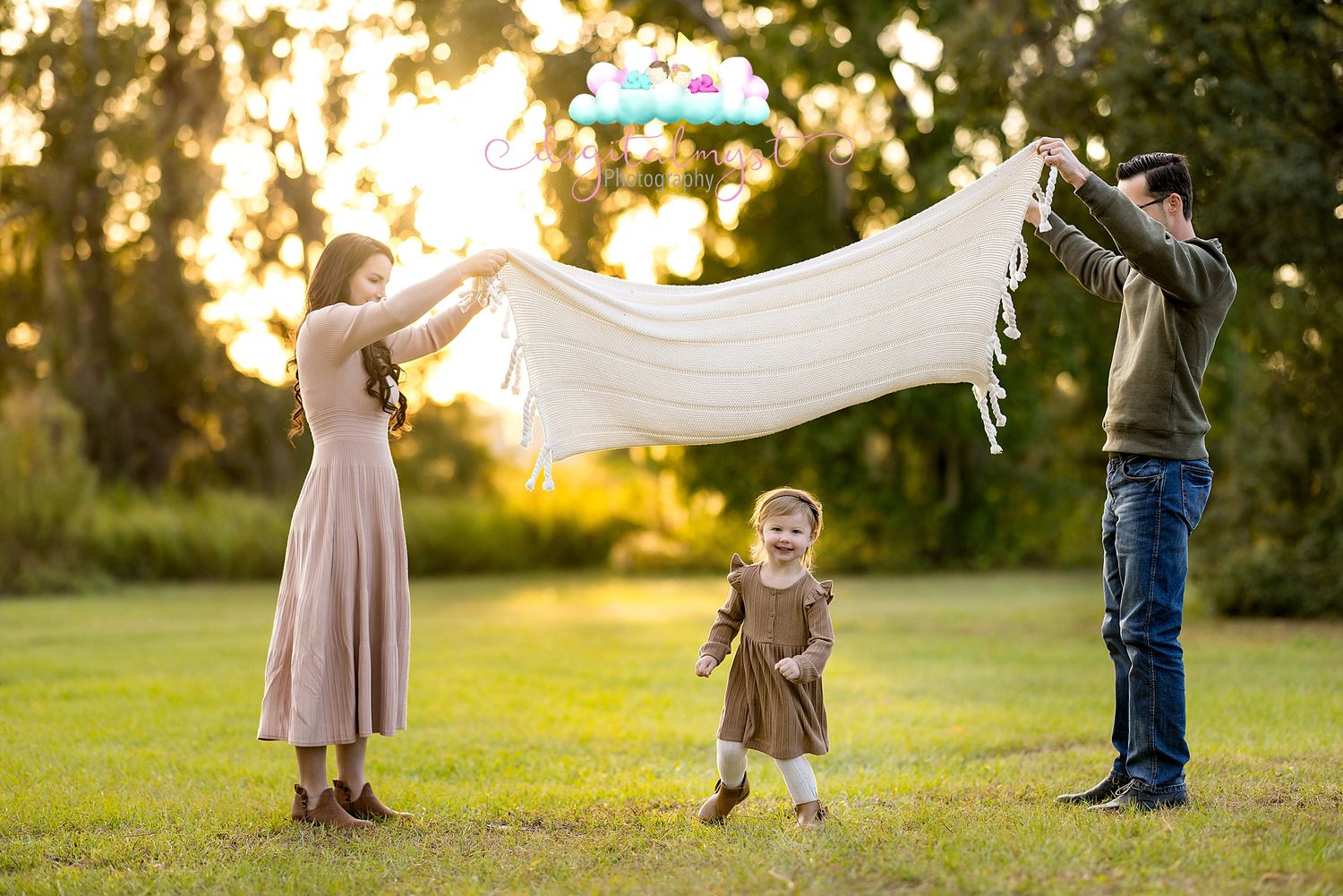 Couple holds flowing white fabric in golden sunlit field during sunset photo session.