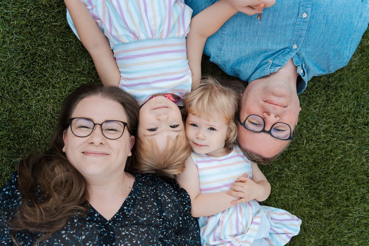 A family lies together on green grass in a series of candid photos showing joyful relaxation during a Rouse hill family photoshoot