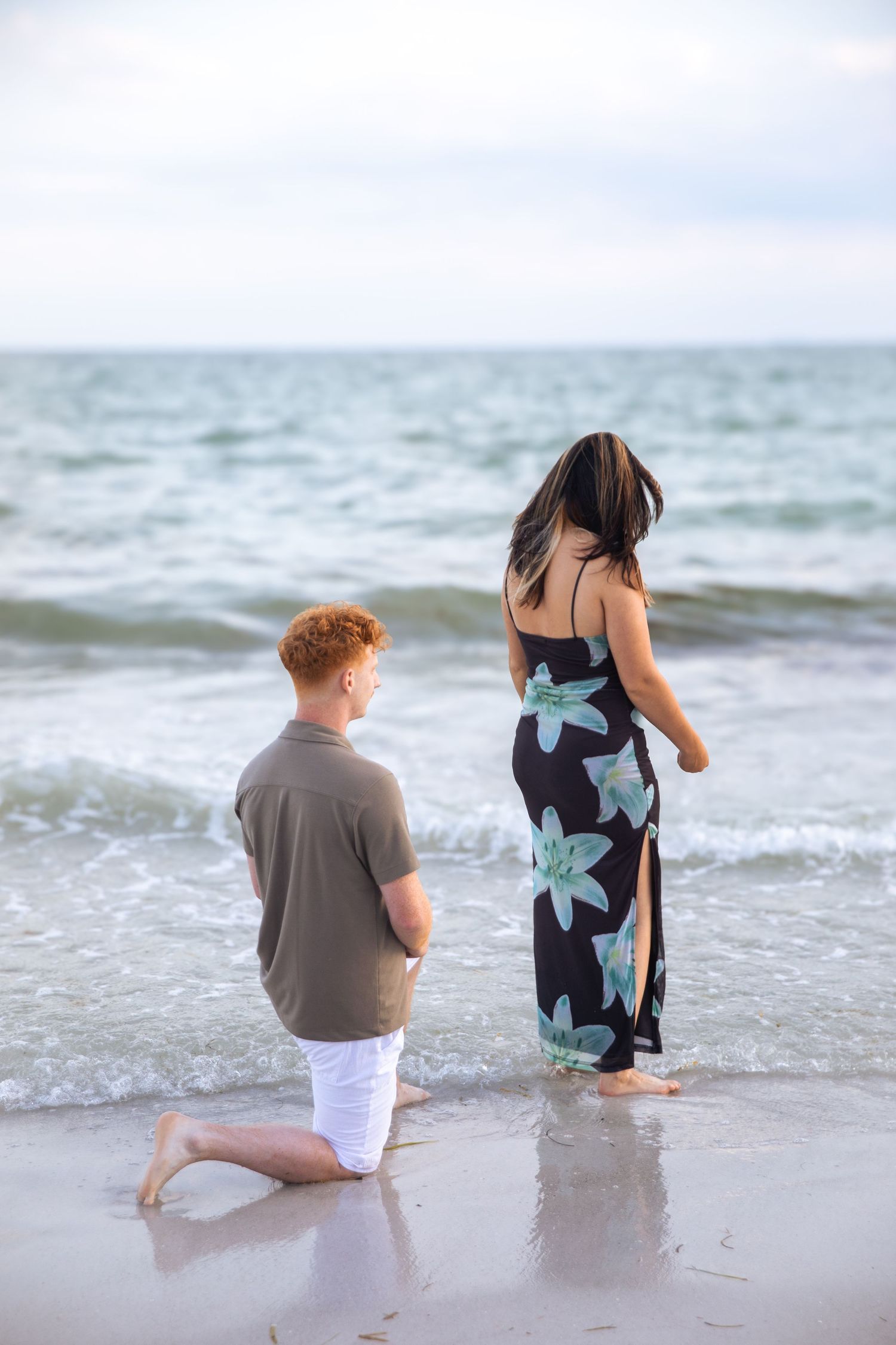 Two hands reaching toward each other at sunset beach, woman wearing diamond engagement ring and bracelet.