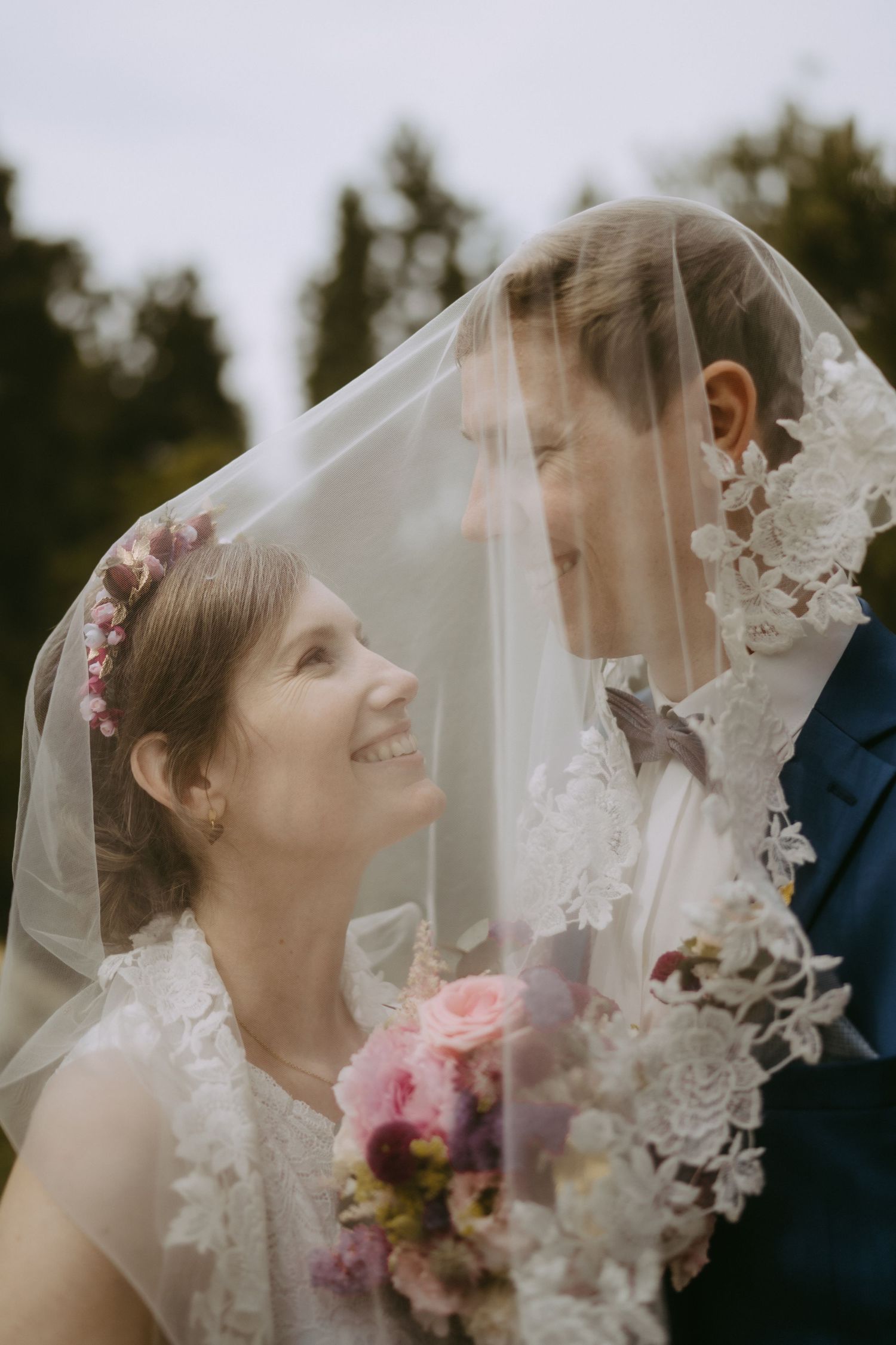 Wedding couple shares intimate moments under a delicate lace veil with pink floral accents.