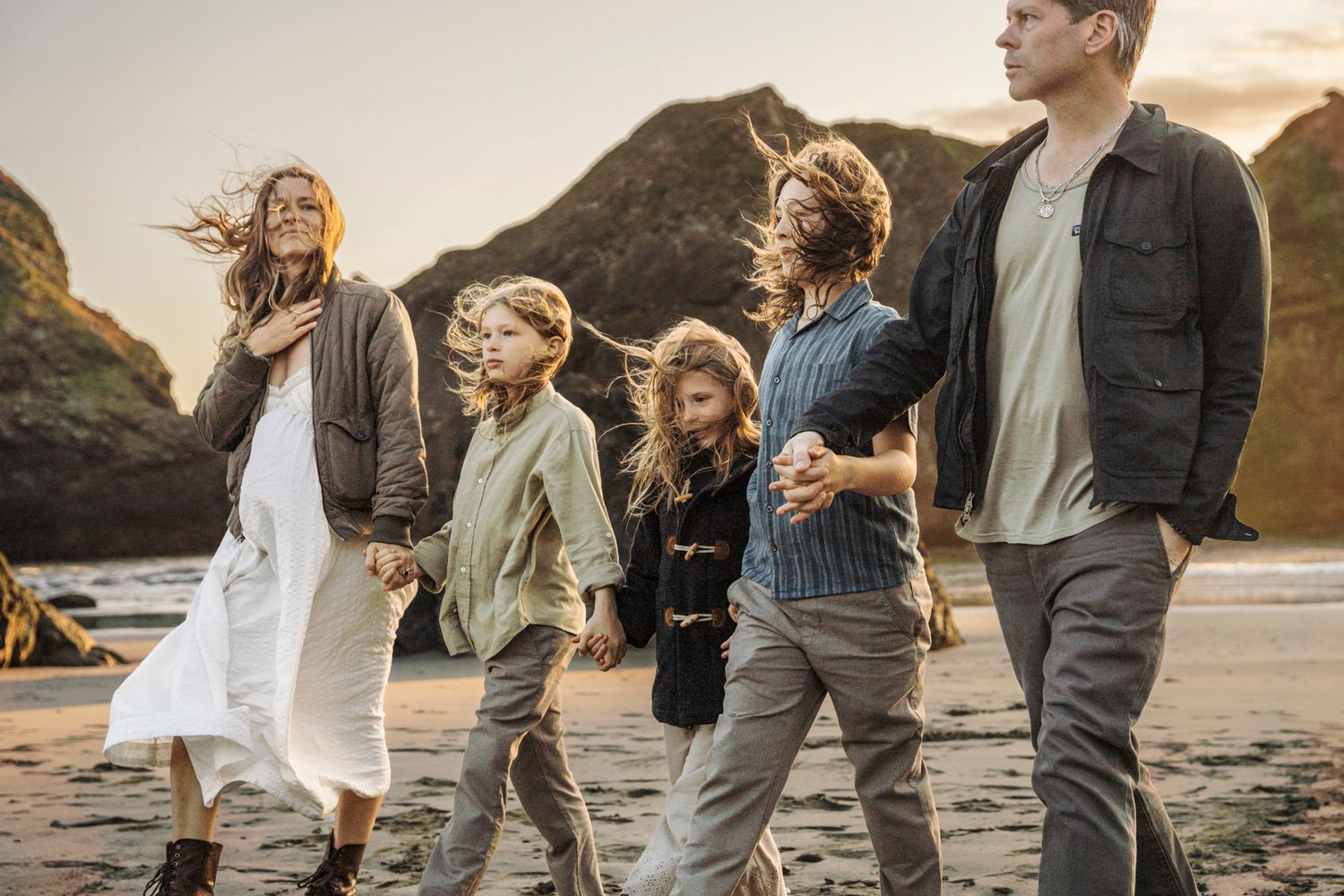 Family dressed in casual clothes walking hand in hand together on a scenic beach at sunset photo session