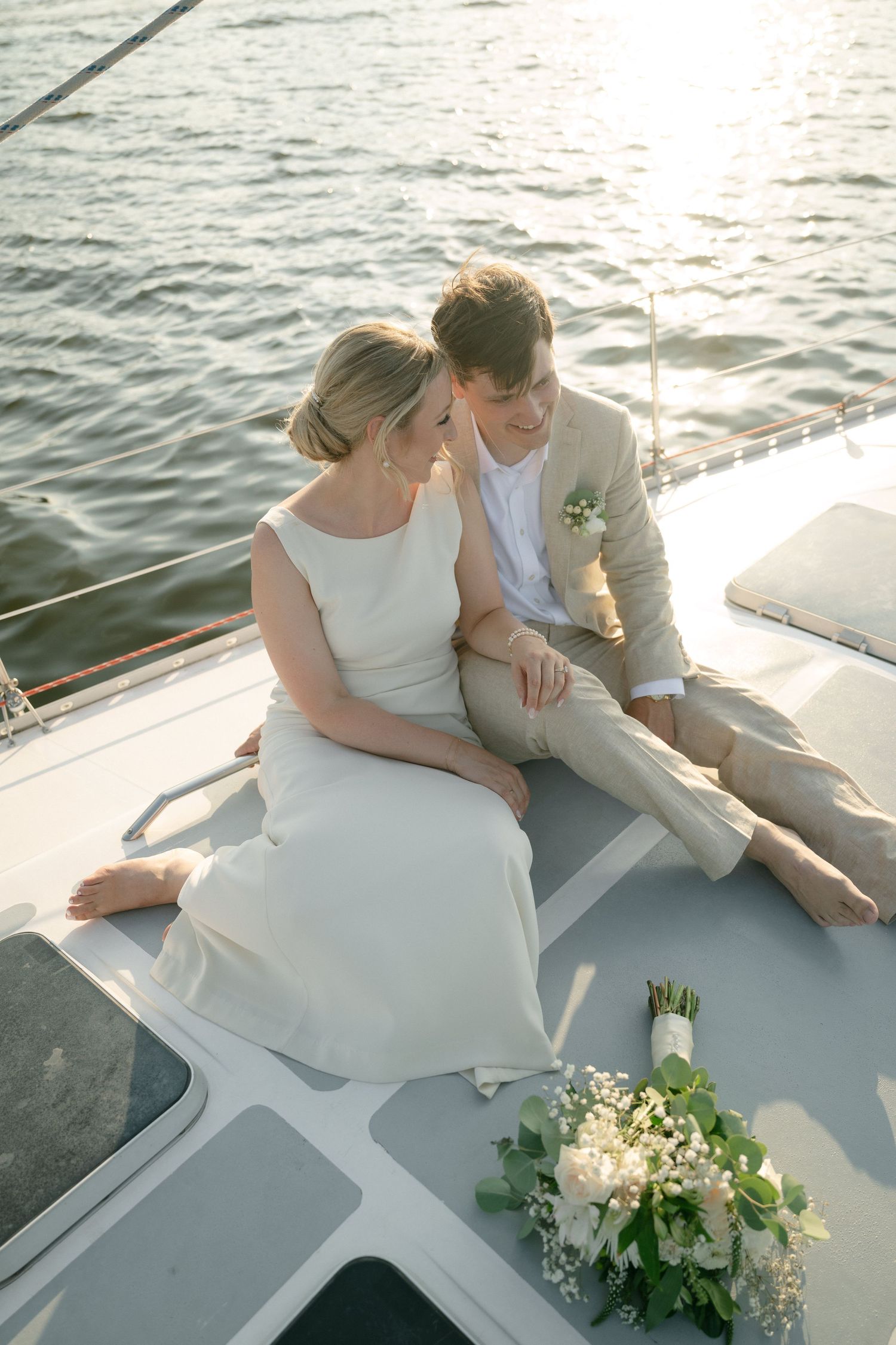 A romantic scene aboard a boat at sunset with a wedding bouquet of white flowers and greenery on deck.