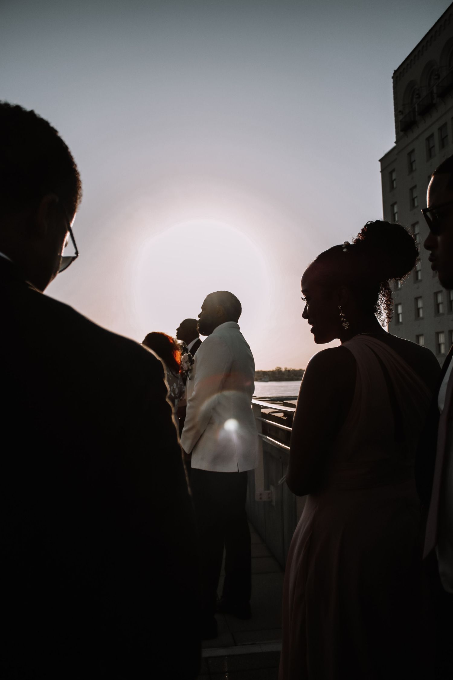 Silhouette of wedding guests against sunset sky on outdoor terrace.