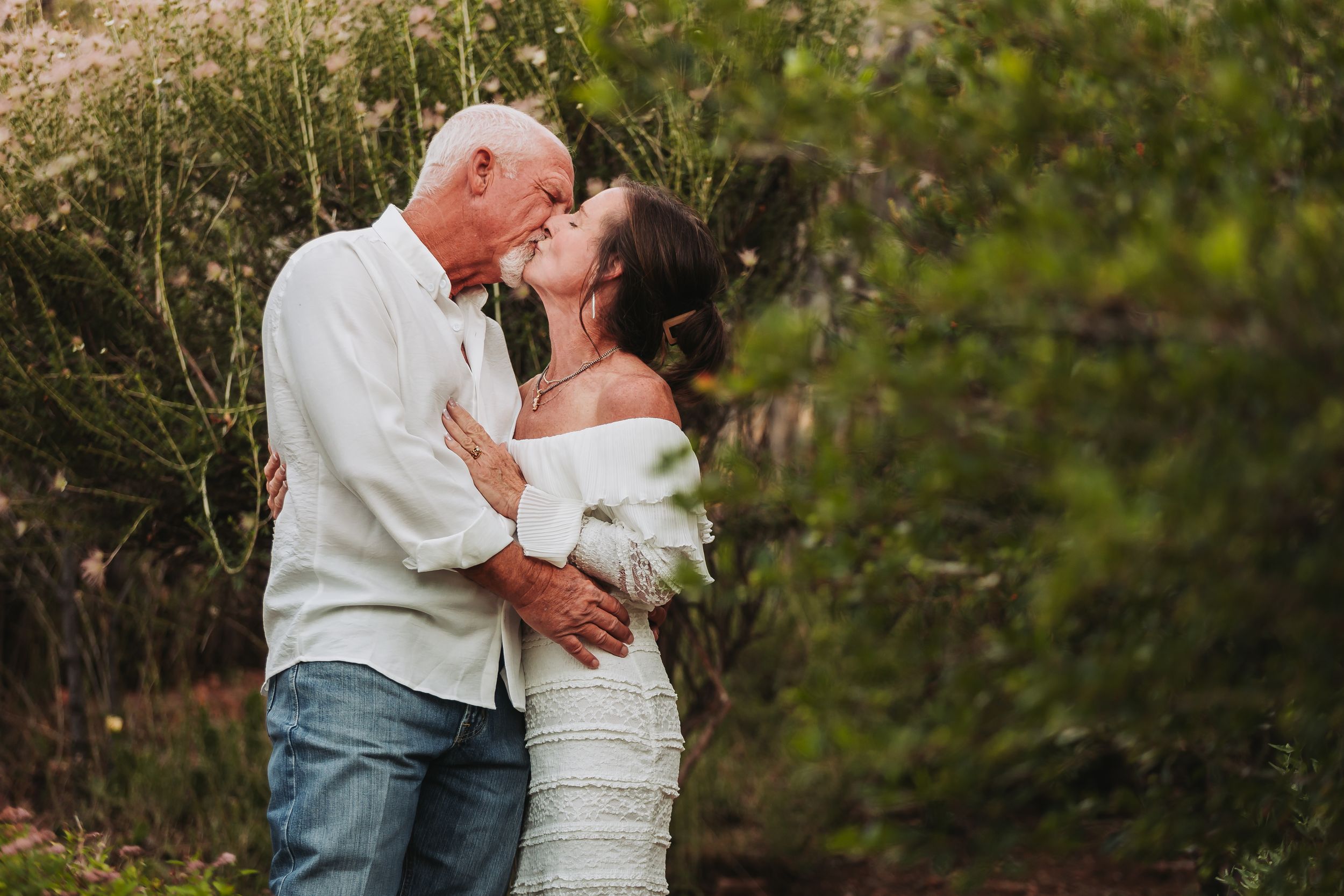 An intimate outdoor portrait photo of a couple embracing and sharing a tender romantic moment in a natural setting.