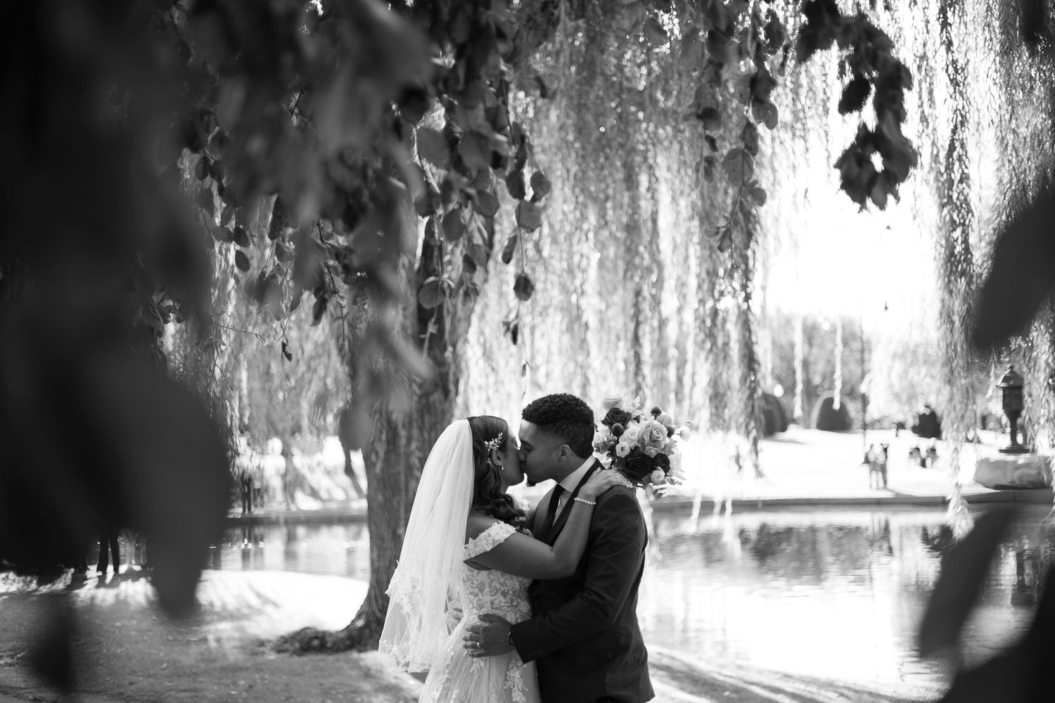A romantic couple shares a tender moment under a willow tree in a dreamy black and white photograph.