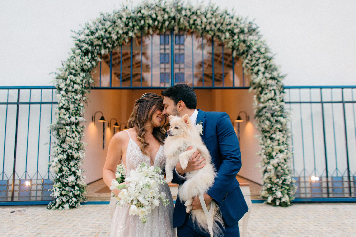 A series of romantic wedding moments on a balcony decorated with white floral arrangements and blue railings.