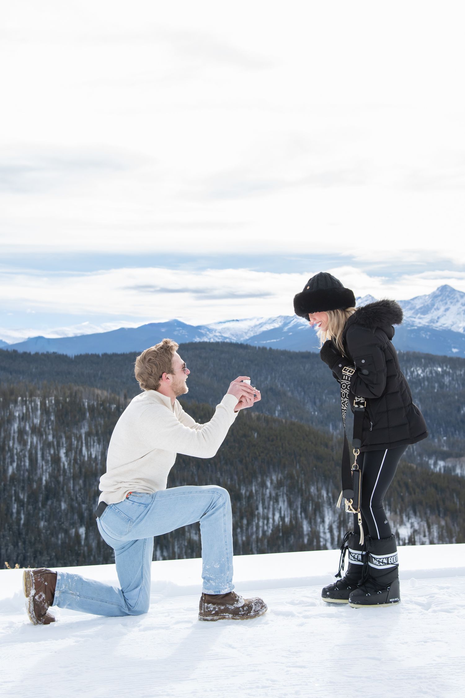Man is down on one knee proposing to a stylish woman with mountains and snow around them in Vail Colorado.