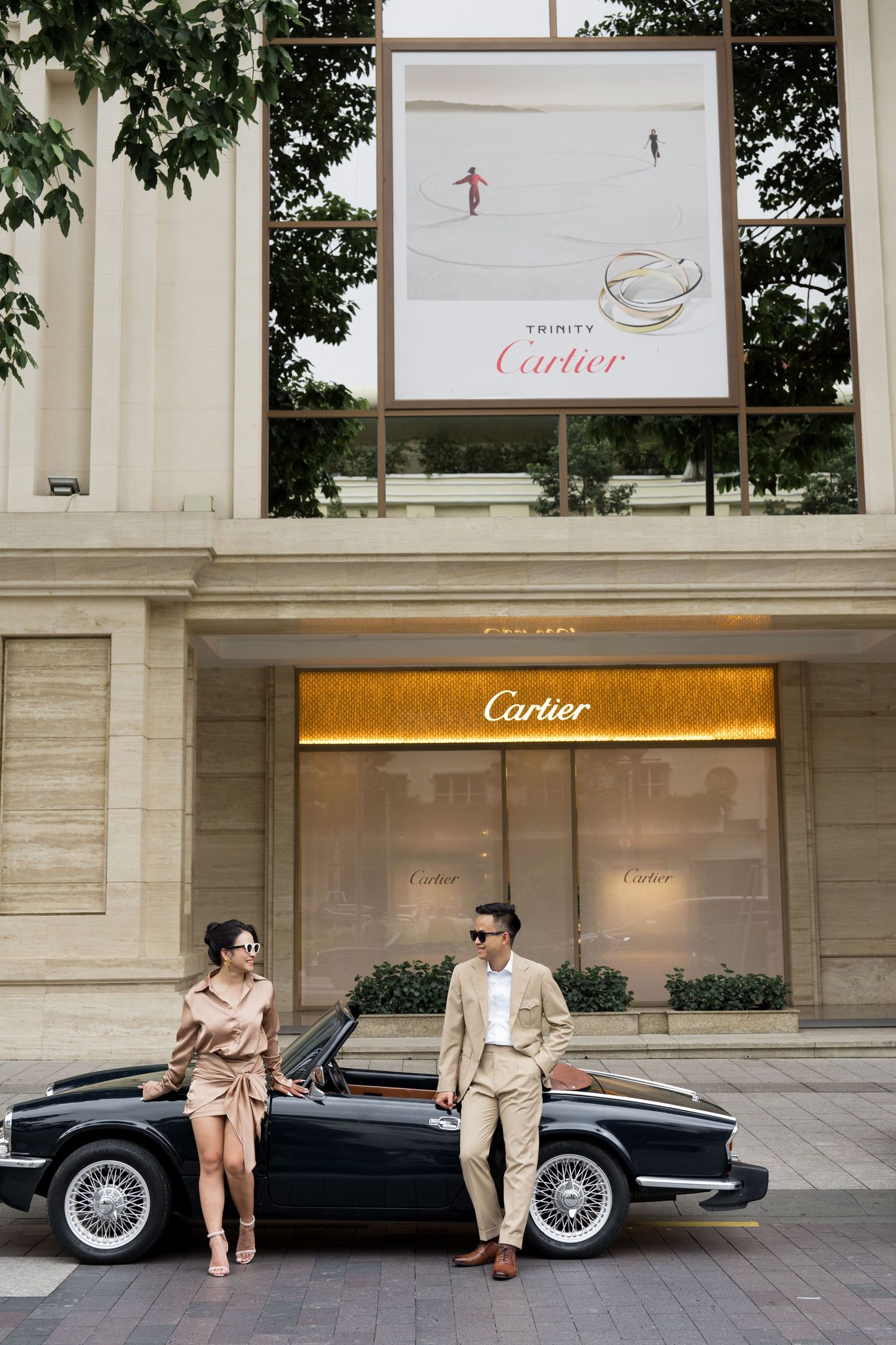 Elegant couple posing in front of a Cartier luxury boutique beside a classic black convertible car.