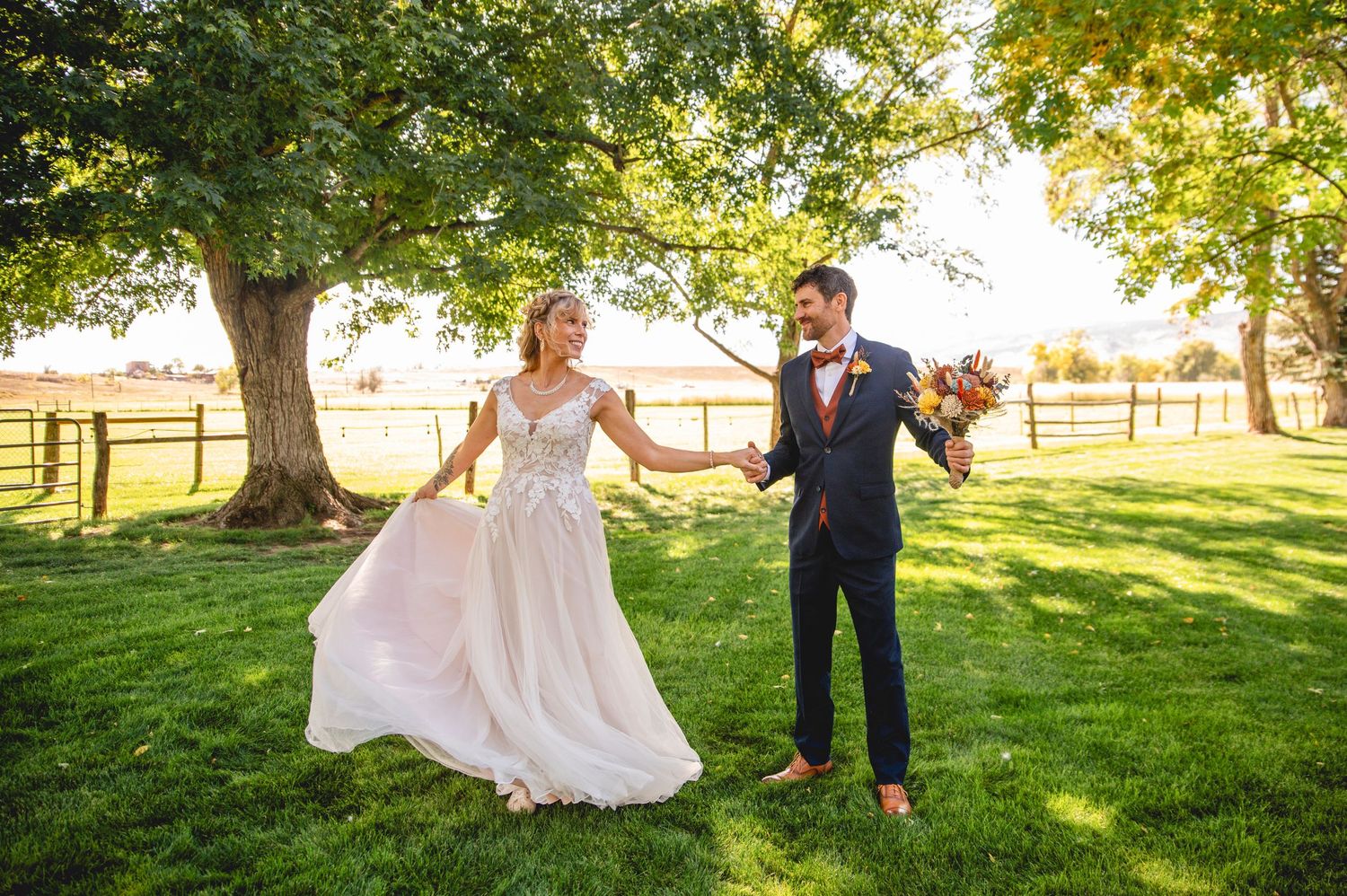A couple dances together on a grassy lawn surrounded by trees during a summer wedding celebration.
