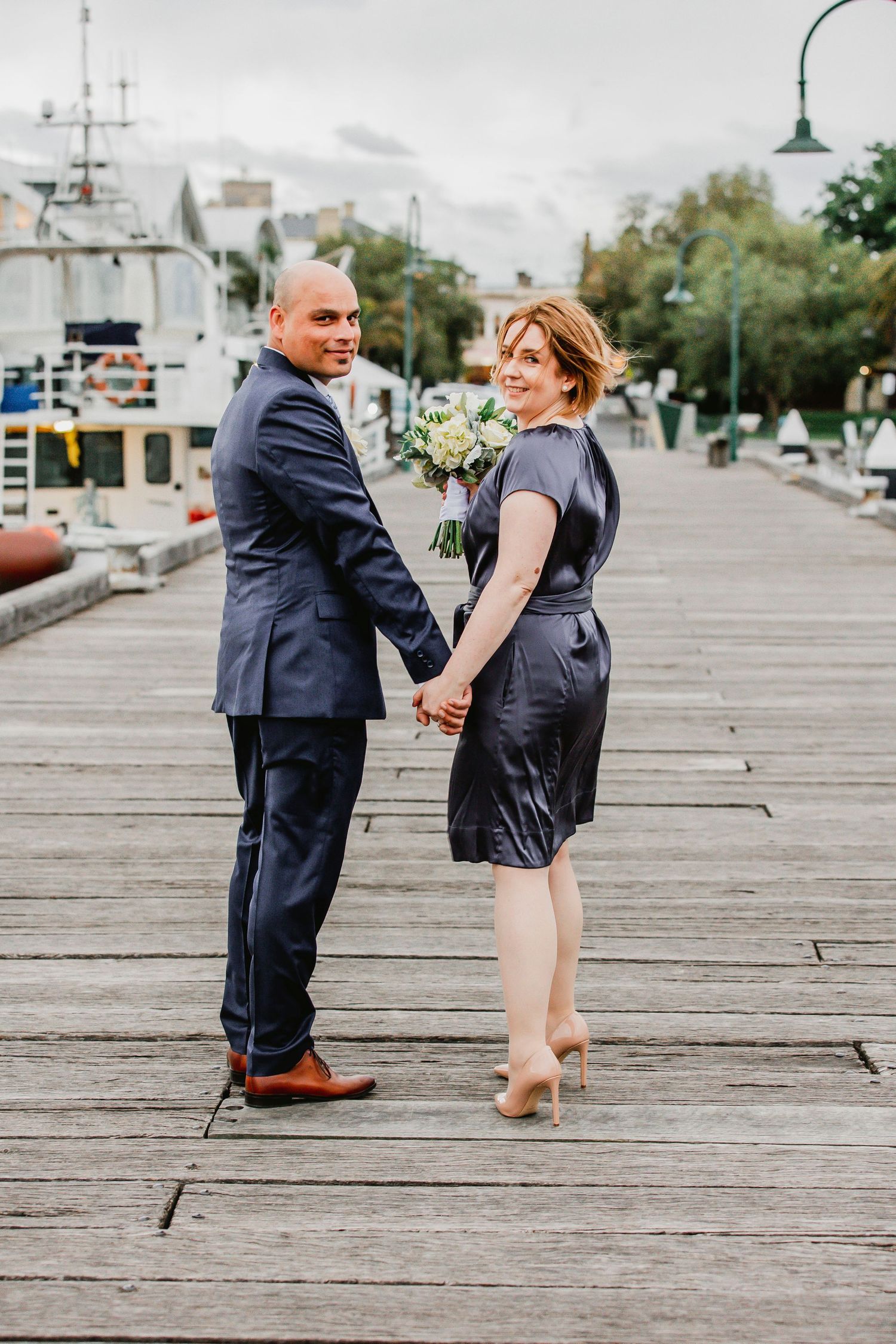 A couple shares a playful moment dancing together on a wooden boardwalk by the water.