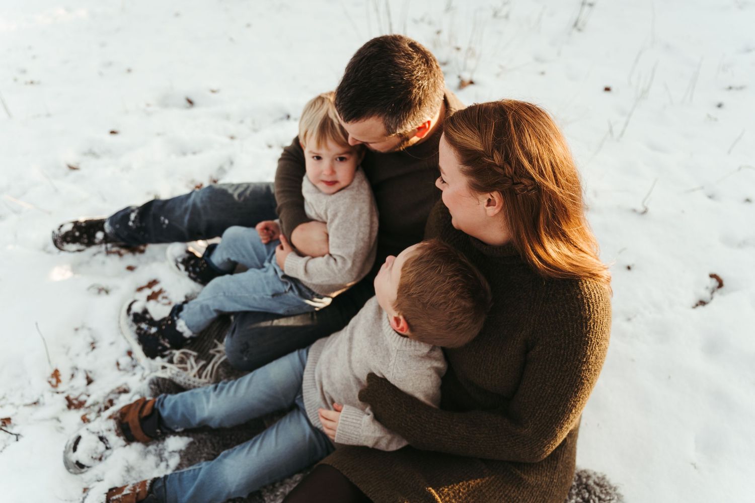 A couple sits together on snowy ground while sharing a romantic winter moment outdoors.