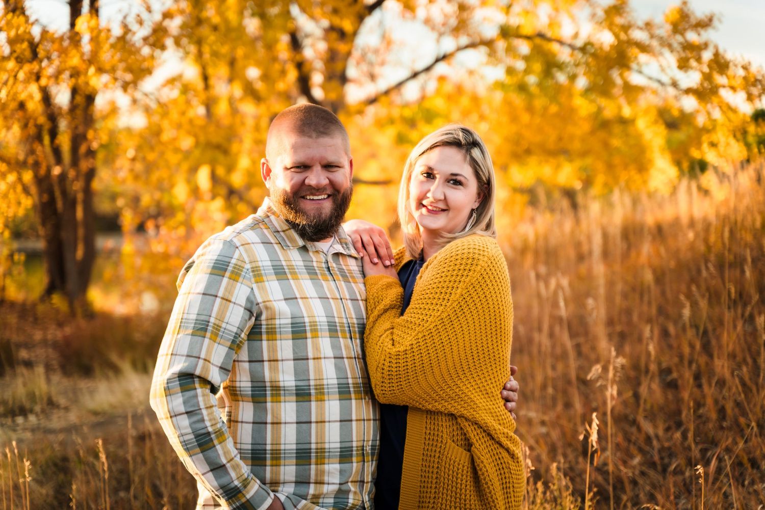 A couple shares a joyful moment together during an autumn photoshoot with golden foliage in the background.