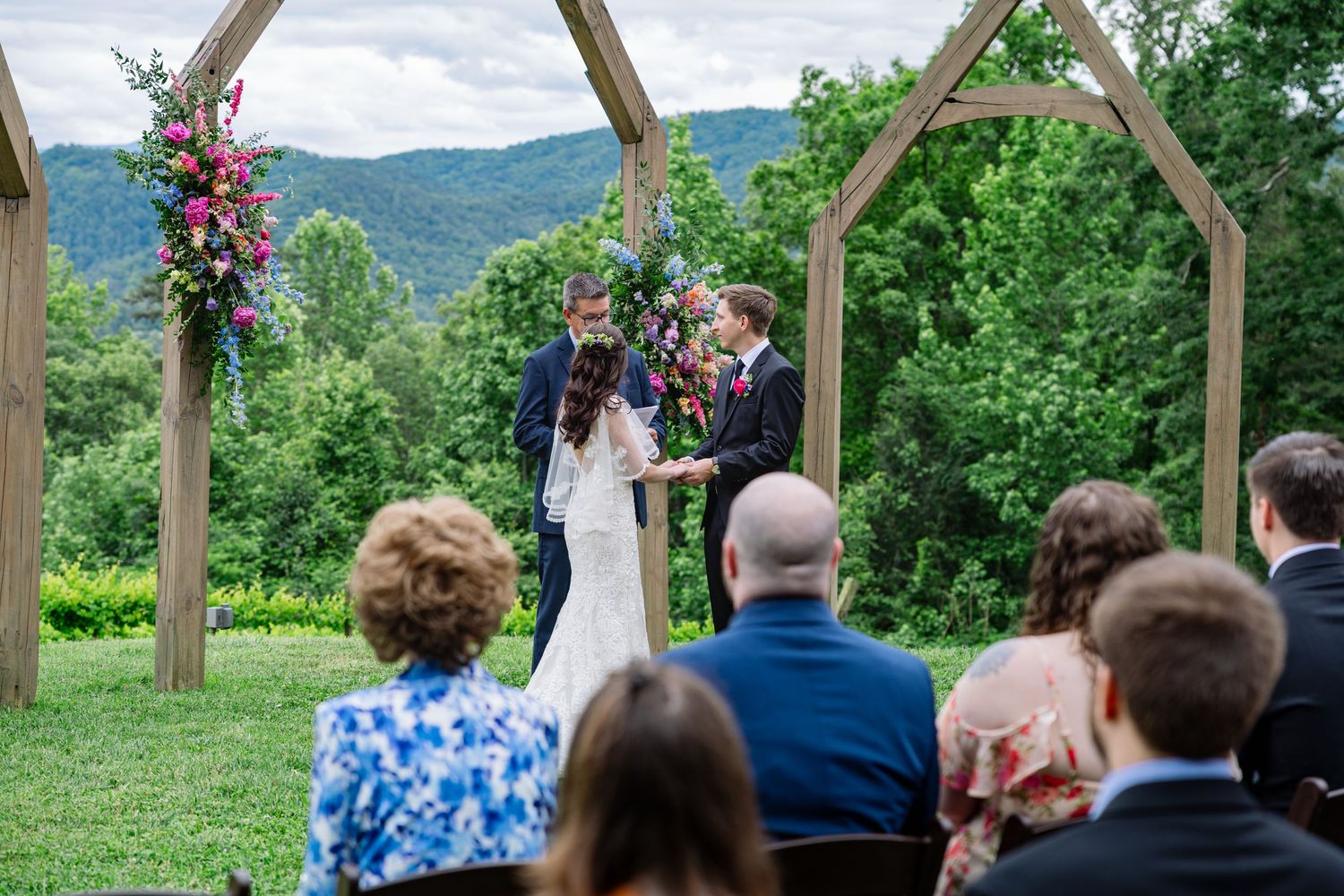 Outdoor wedding ceremony under a rustic wooden pergola with mountain views and floral decorations.