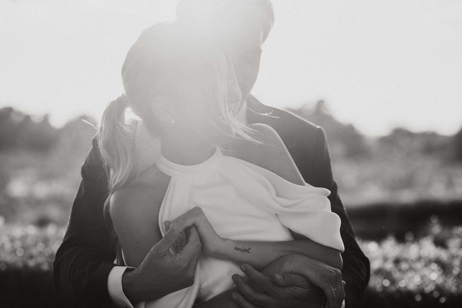 Black and white intimate photo of person holding newborn baby wrapped in blanket with sunlight behind them.