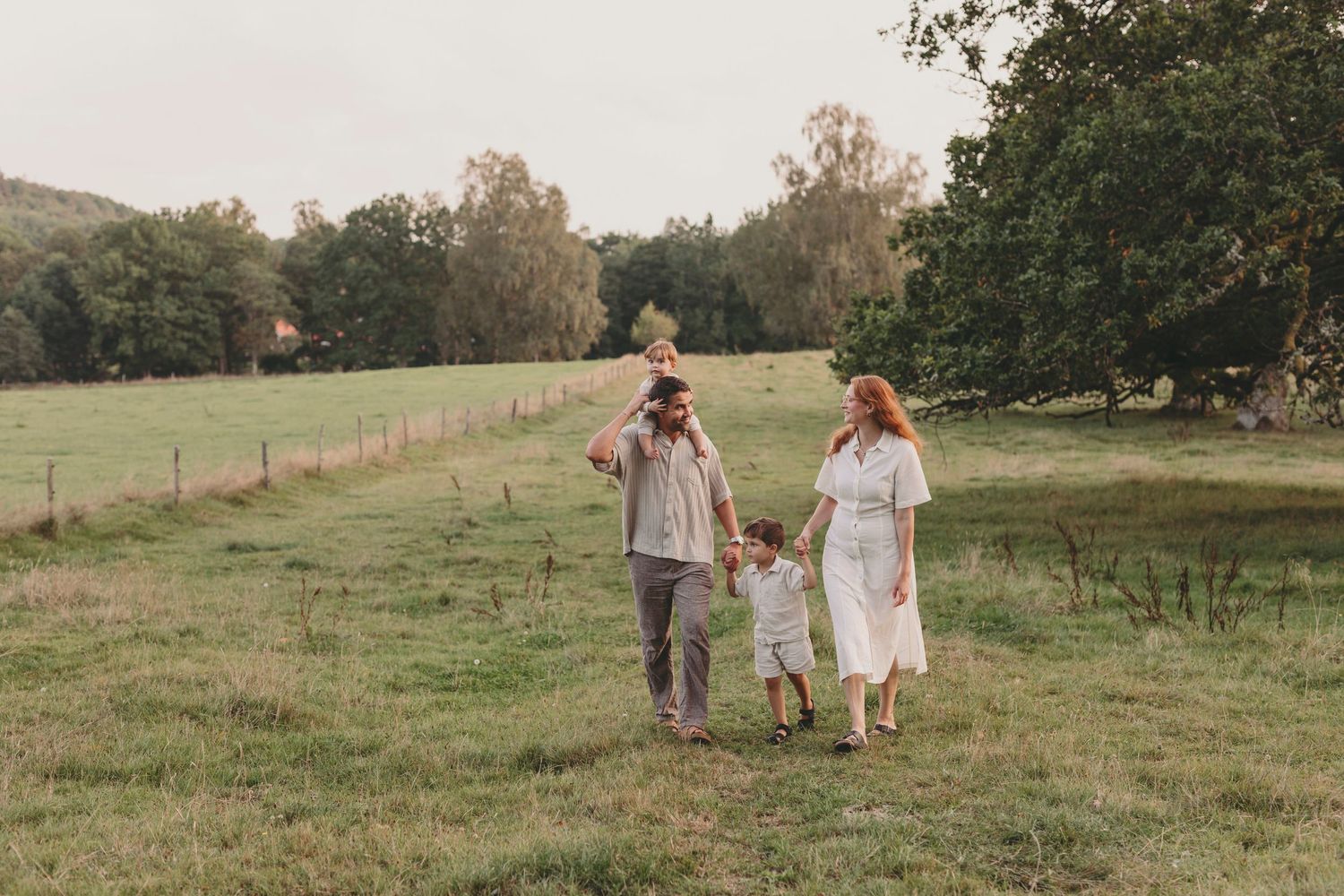 A couple walks hand in hand with a small child through a serene pastoral meadow at golden hour.