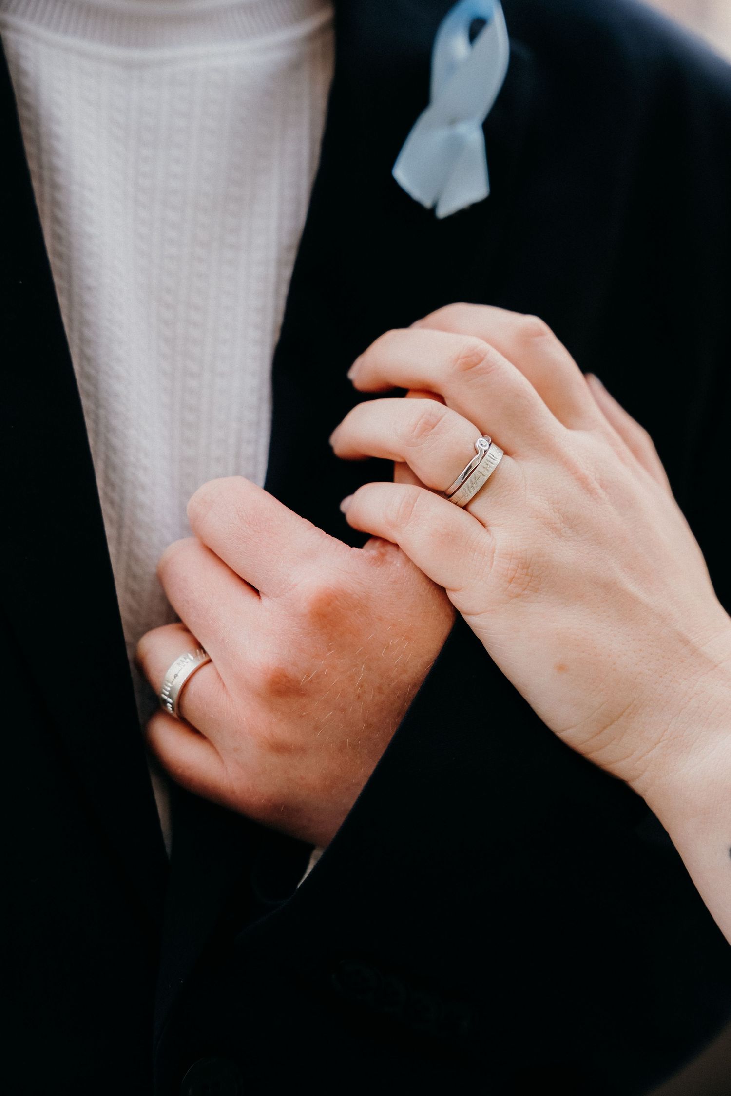 Close-up view of hands wearing wedding rings against a white dress and dark background.